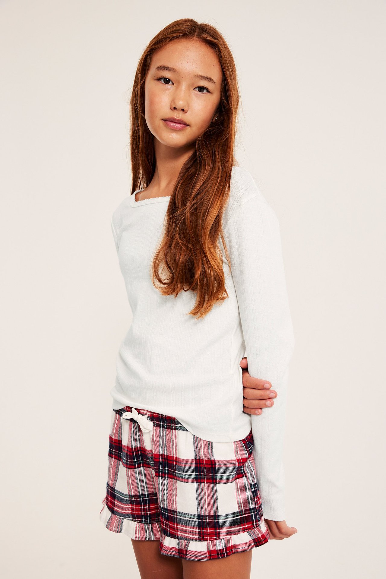 Framsida av ett barn i en offwhite långärmad pointelle pyjamastopp och rutiga shorts.