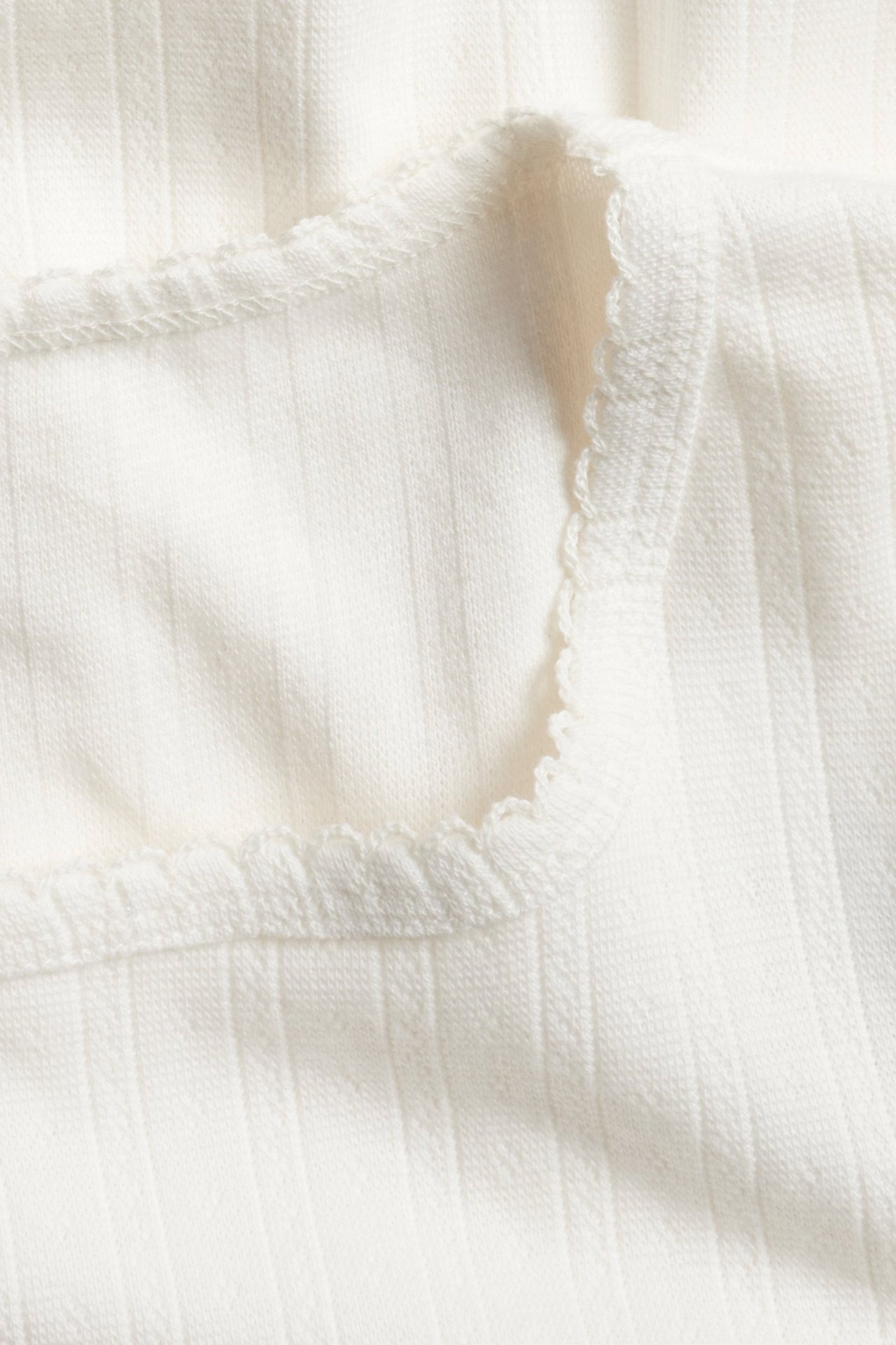 Zbliżenie na kremowobiałą piżamową bluzkę z długim rękawem pointelle z delikatnym wykończeniem picot.