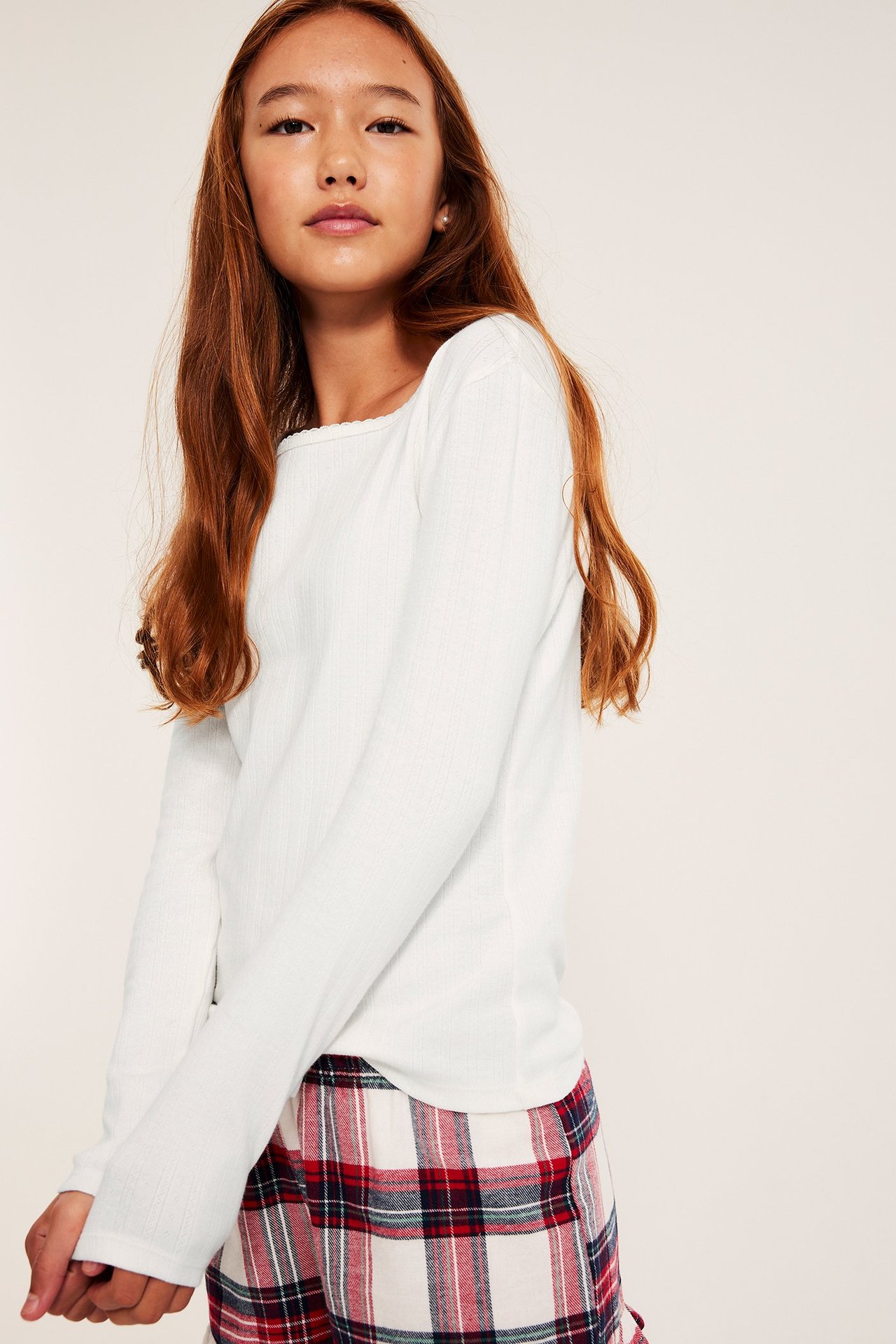 Framifrån: Barn bär en off-white långärmad pointelle pyjamastopp med picotkant och rutiga pyjamasshorts.