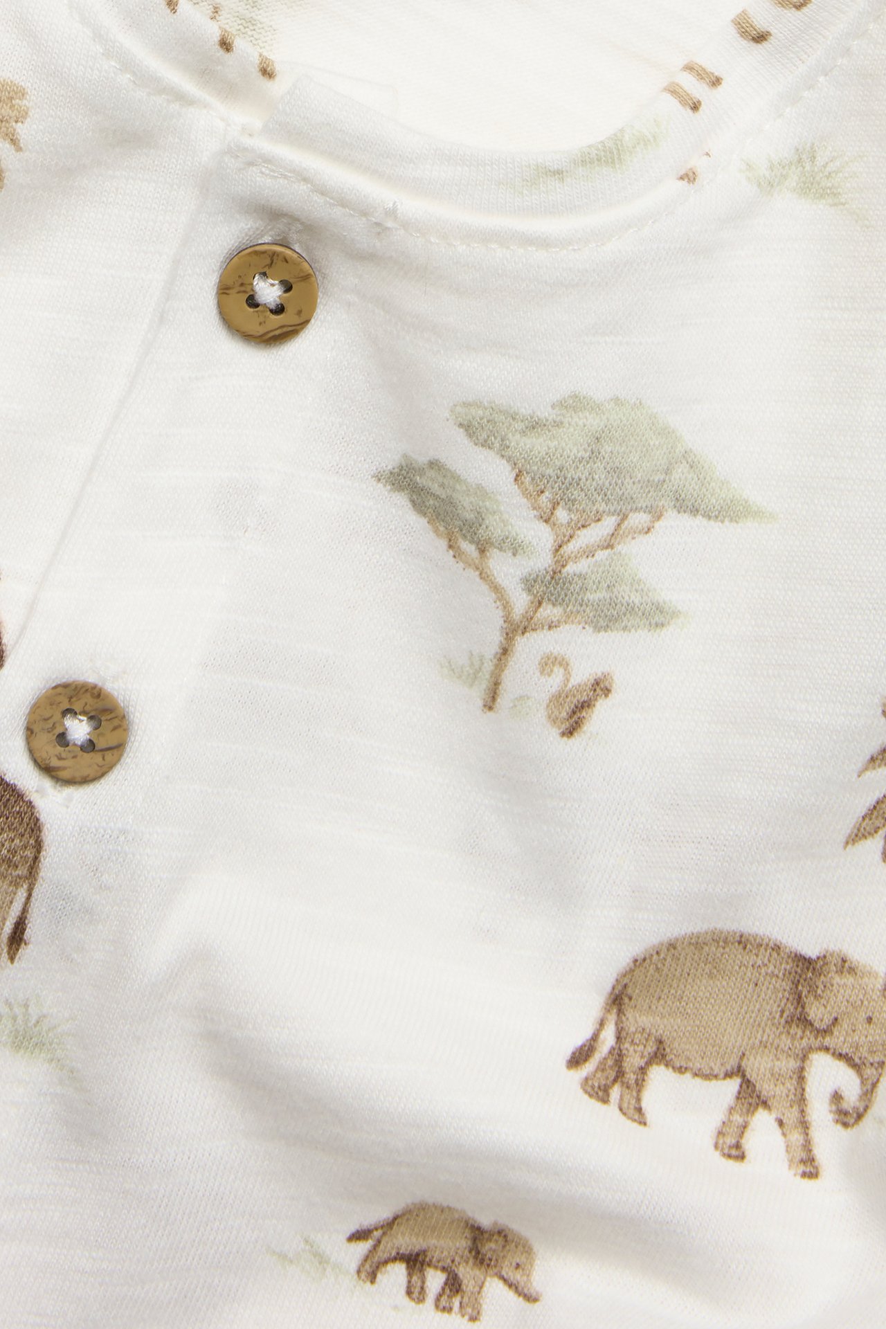Närbild på en offwhite babyplaysuit i slubtrikå med brunt elefantmönster och bruna knappar.
