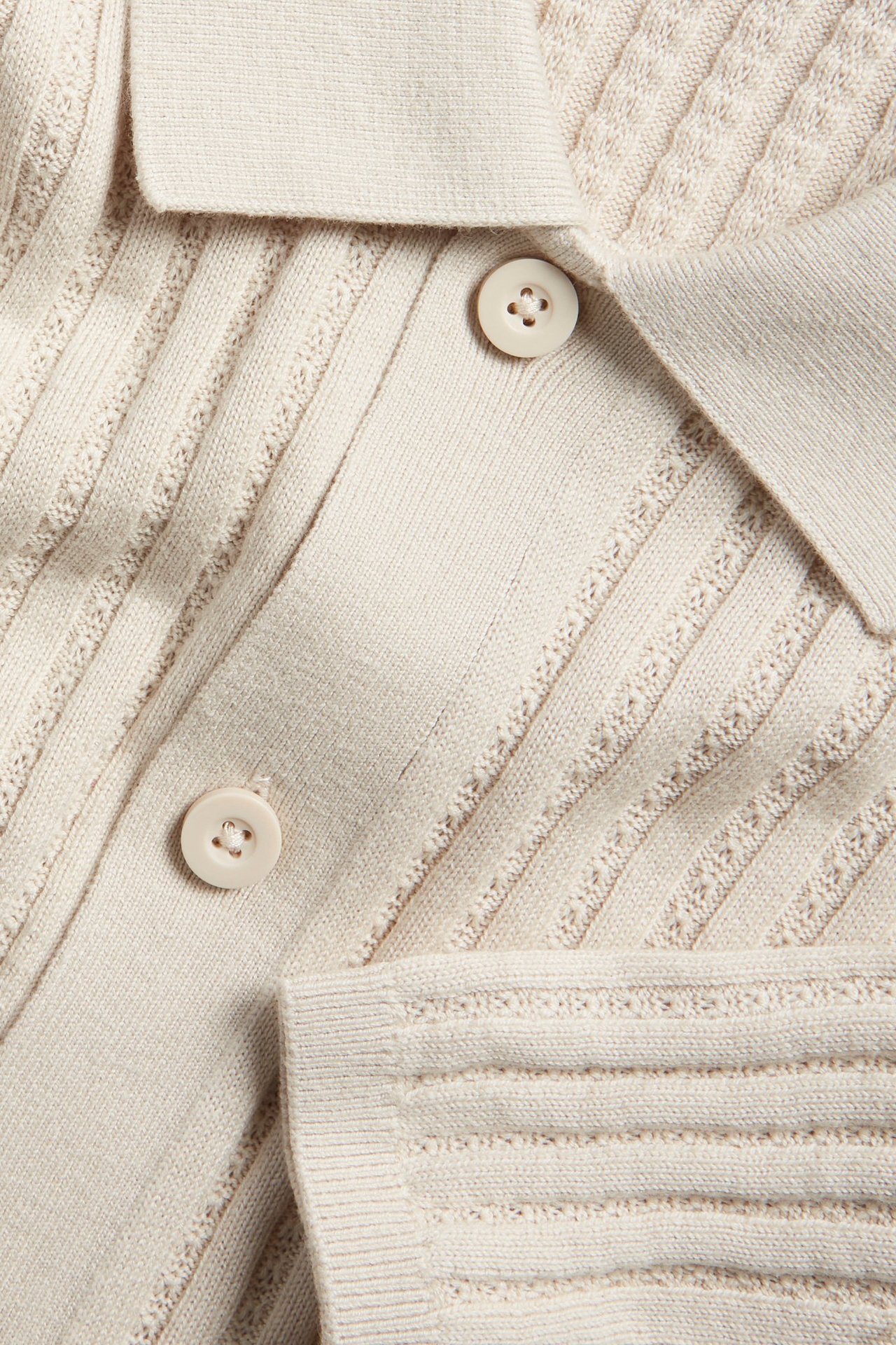 Zbliżenie na jasnobeżowy sweter z dzianiny o prążkowanej strukturze i guzikach z przodu.
