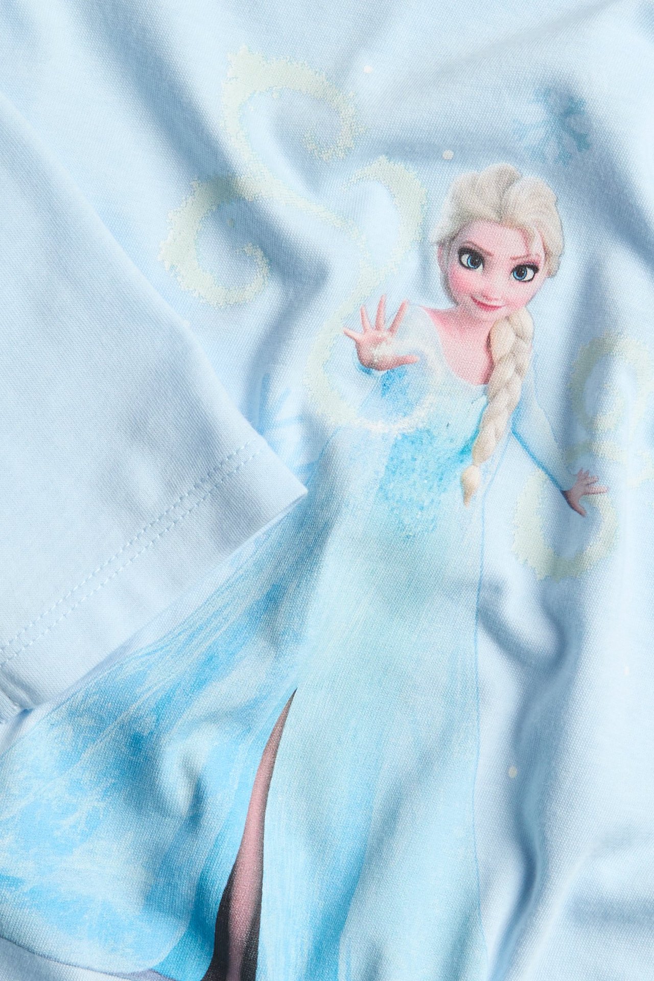 Närbild av en ljusblå långärmad barntopp i bomull med Frost Elsa-tryck framtill.