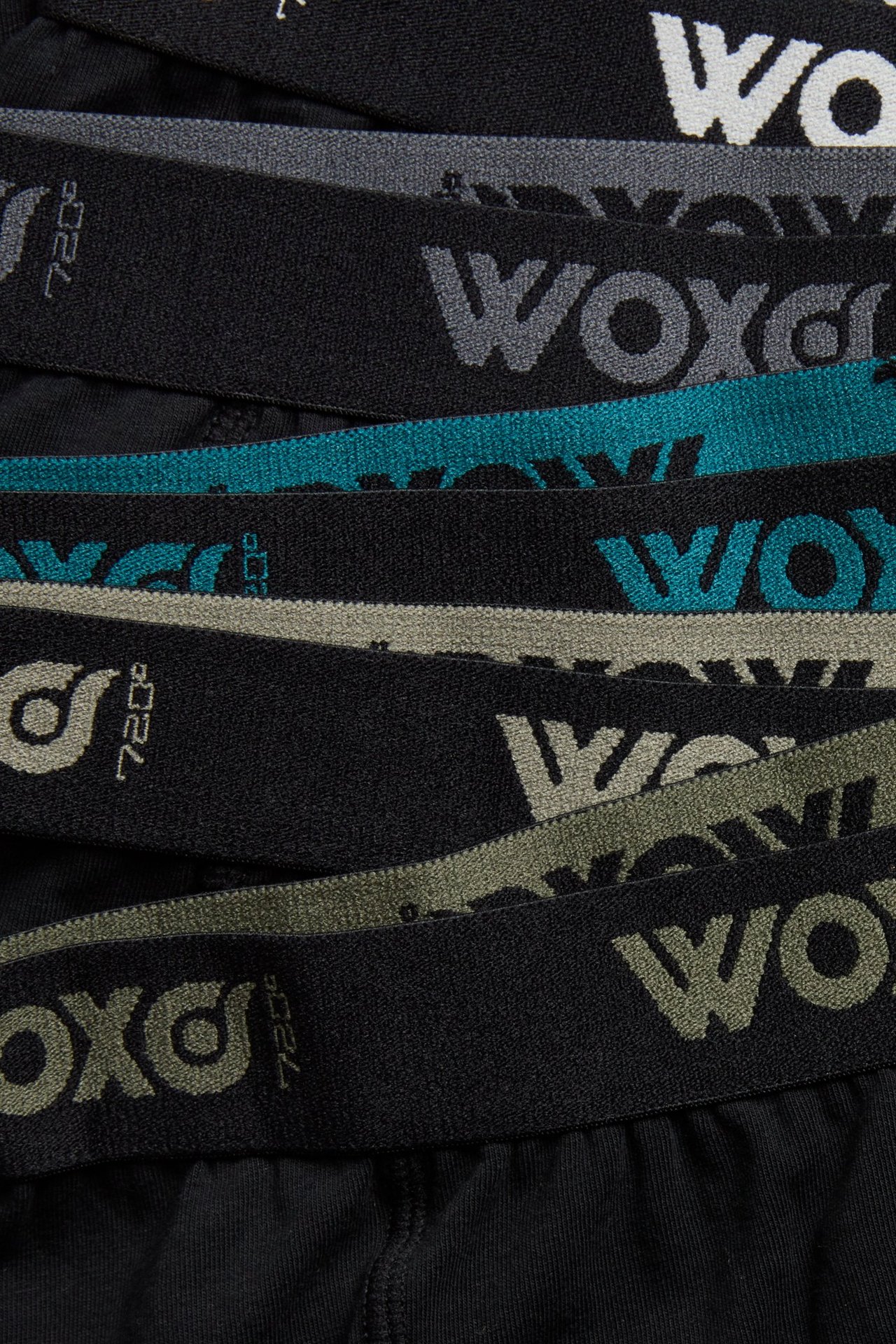 Lähikuva lasten mustista bokserishortseista 5-pakkaus, joissa joustavat vyötärönauhat eri värisellä WOXO-tekstillä.