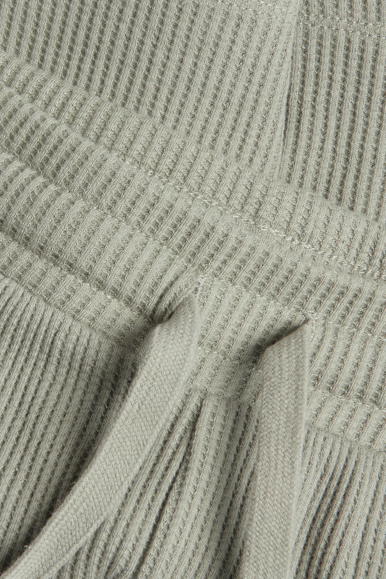 Nærbilde av grønne vaffelstrikkede bomullsshorts med elastisk linning og snøring.