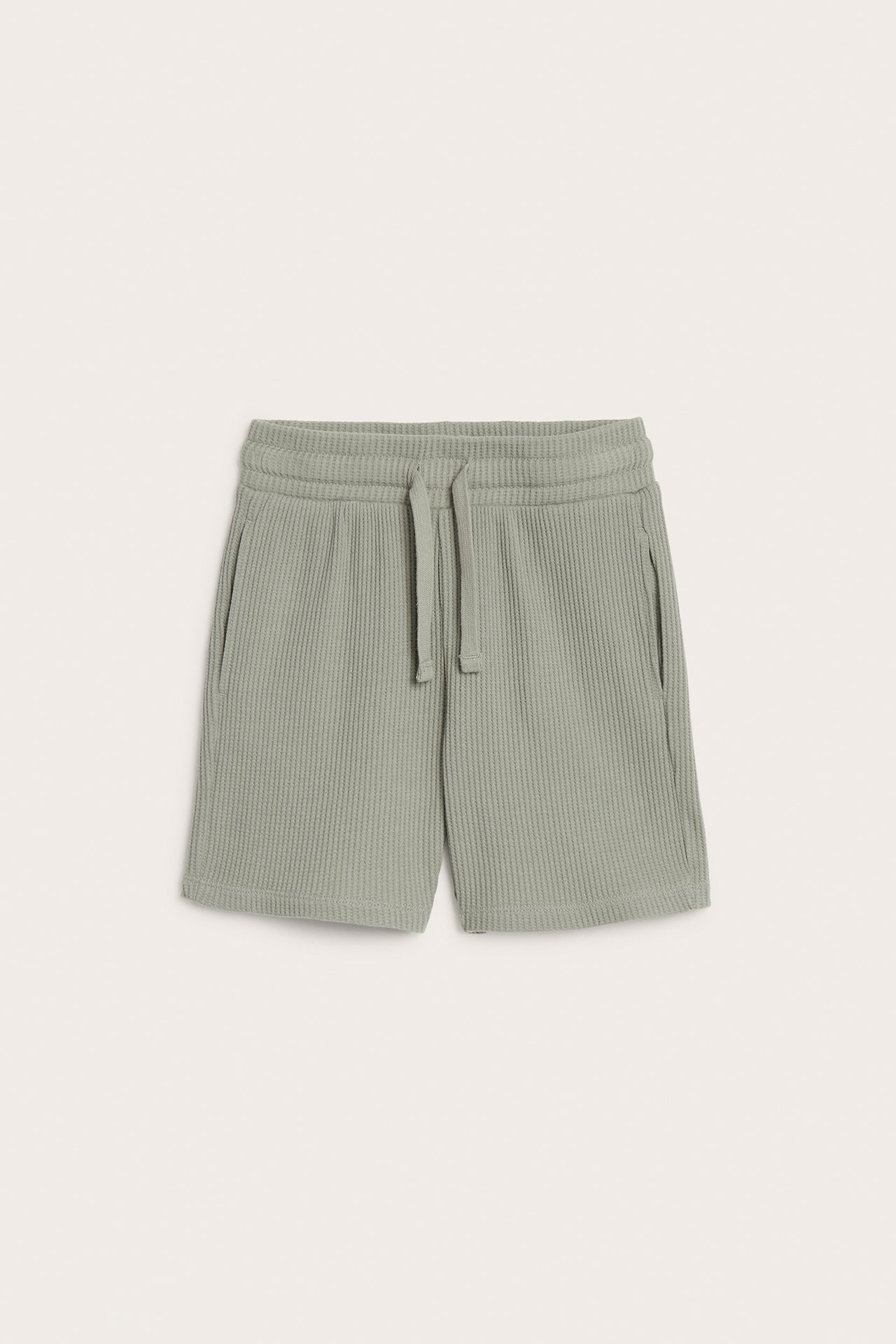 Frontvisning av ensfargede lysegrønne vaffelbomullsshorts med elastisk snøring i midjen og sidelommer.