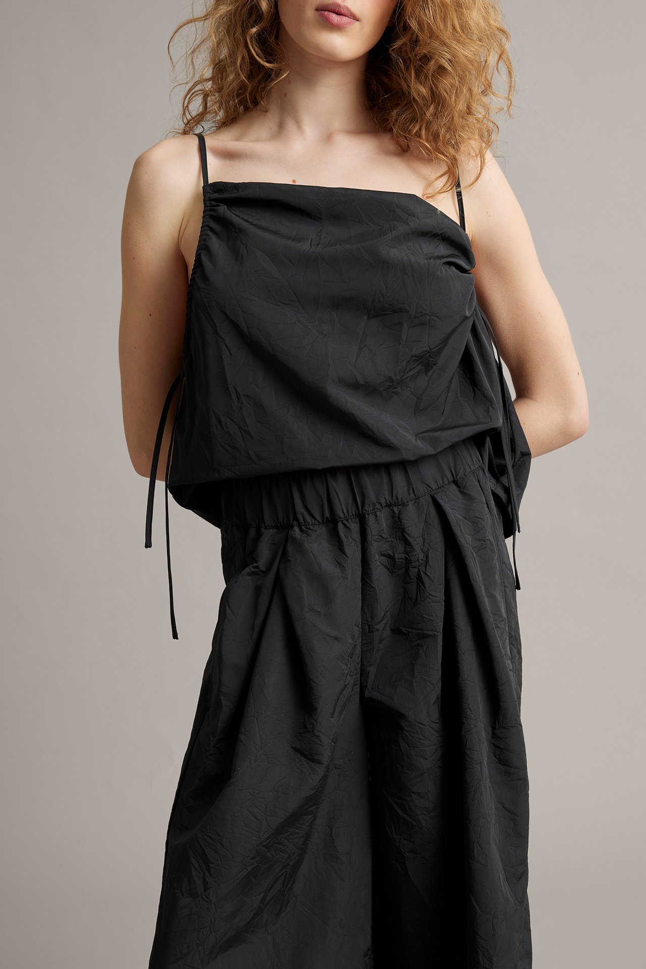 Framifrån, kvinna i svart draperat linne med tunna axelband och matchande svarta vida byxor.