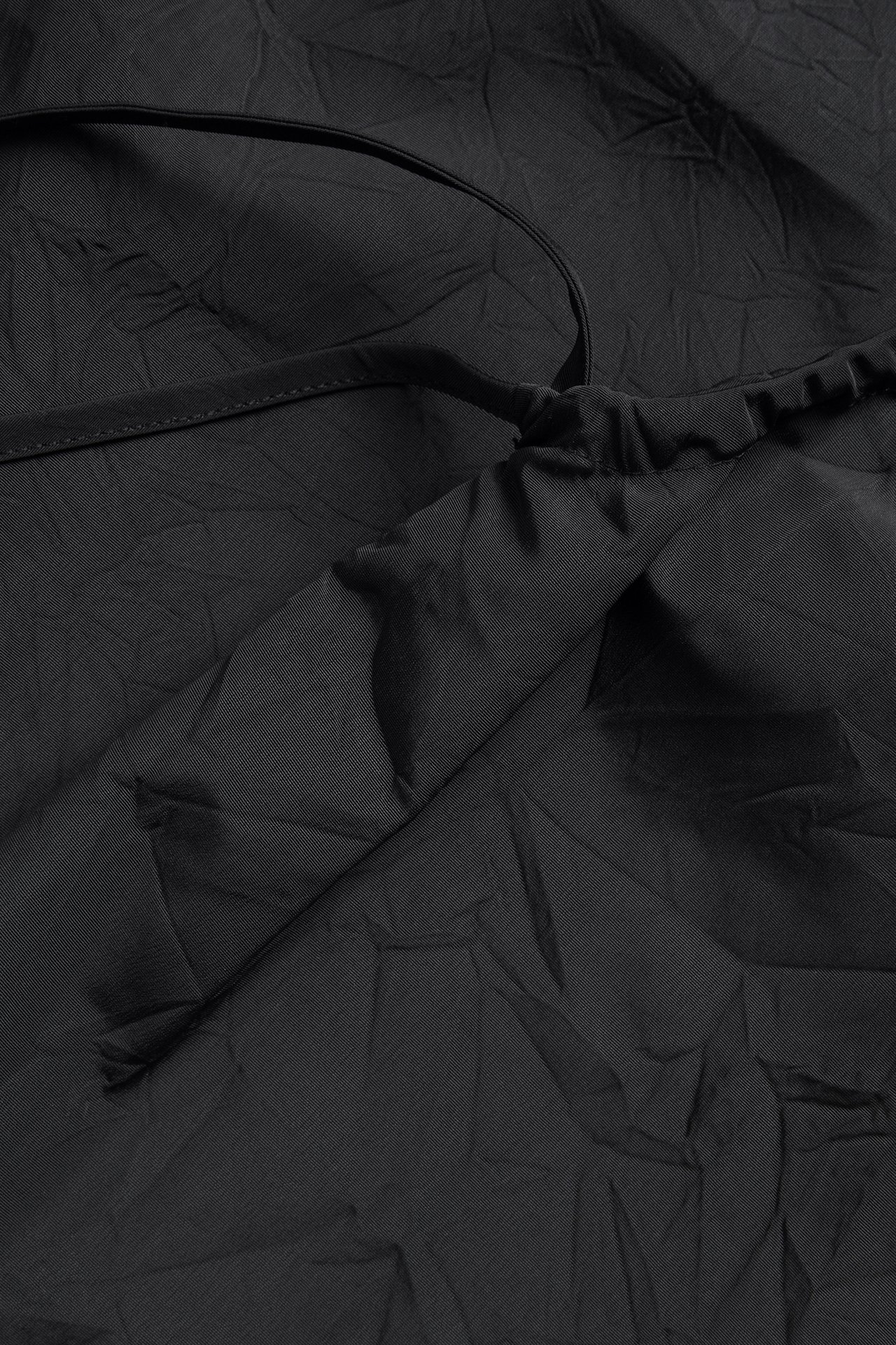 Zbliżenie czarnego, strukturalnego topu z poliestru, z drapowanymi detalami i regulowanym ramiączkiem.