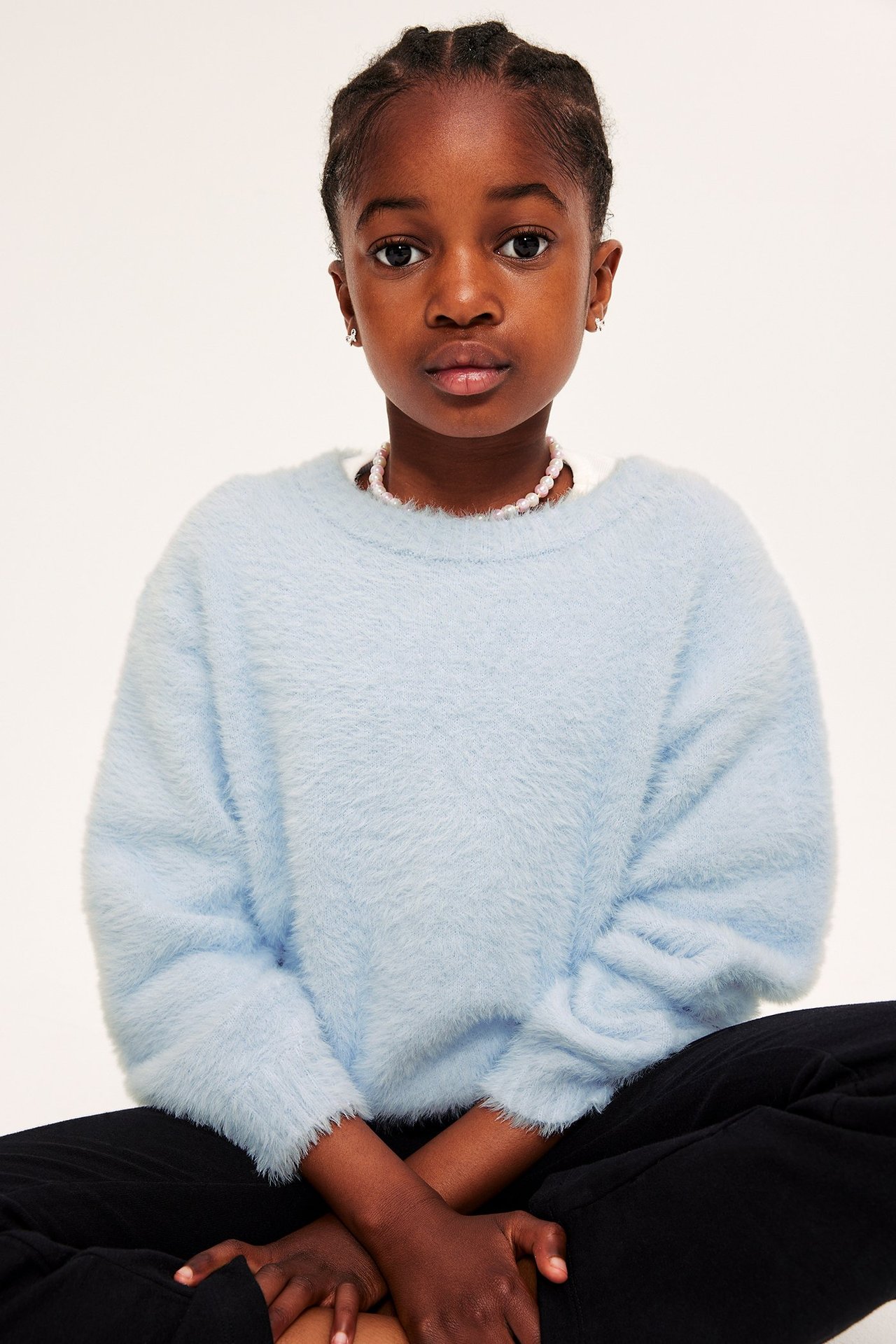 Frontbilde av et barn i lyseblå strikkegenser i feather yarn, rosa perlekjede og svarte bukser.