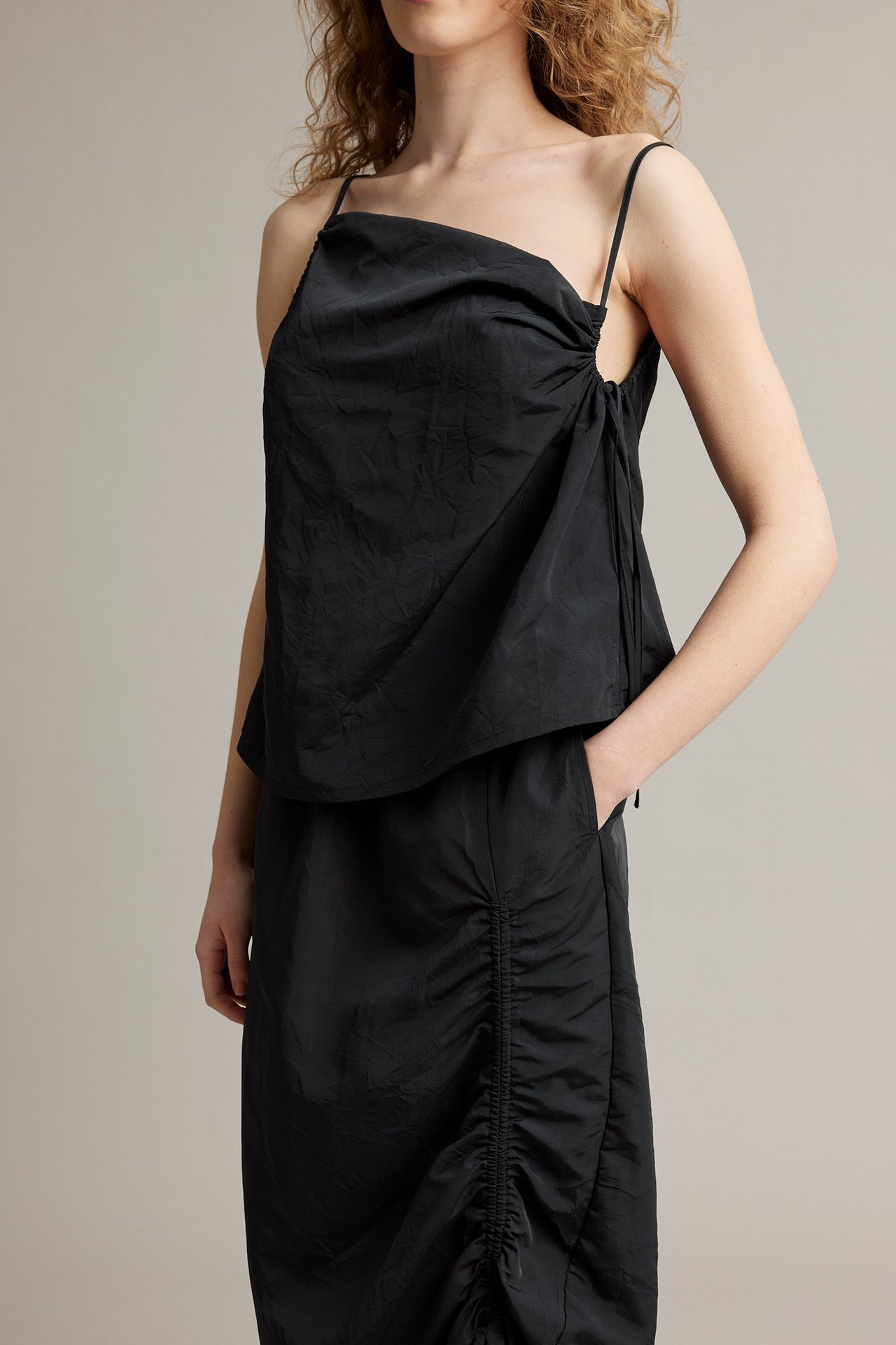 Framifrån, kvinna i svart polyesterkjol med sidodrapering och matchande svart linne.