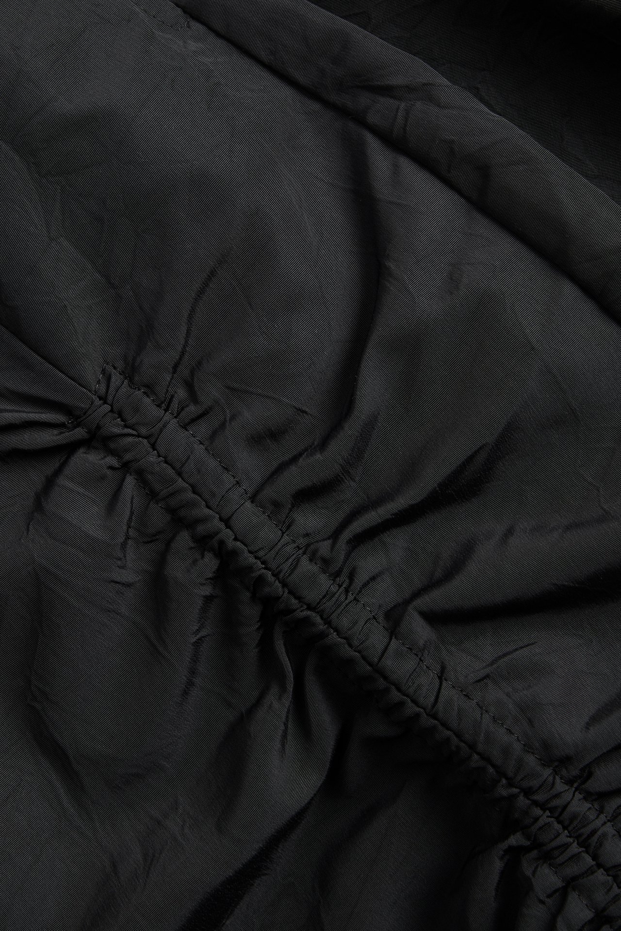 Zbliżenie czarnej spódnicy z marszczonym detalem drapowania wzdłuż ukośnego szwu.