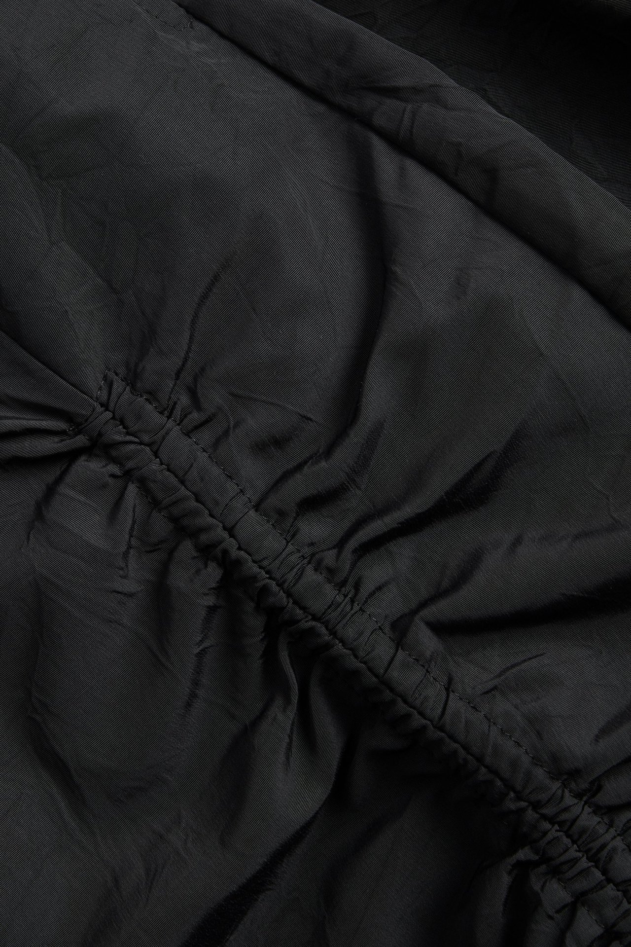 Närbild på en svart kjol med en rynkad draperingsdetalj längs en diagonal söm.