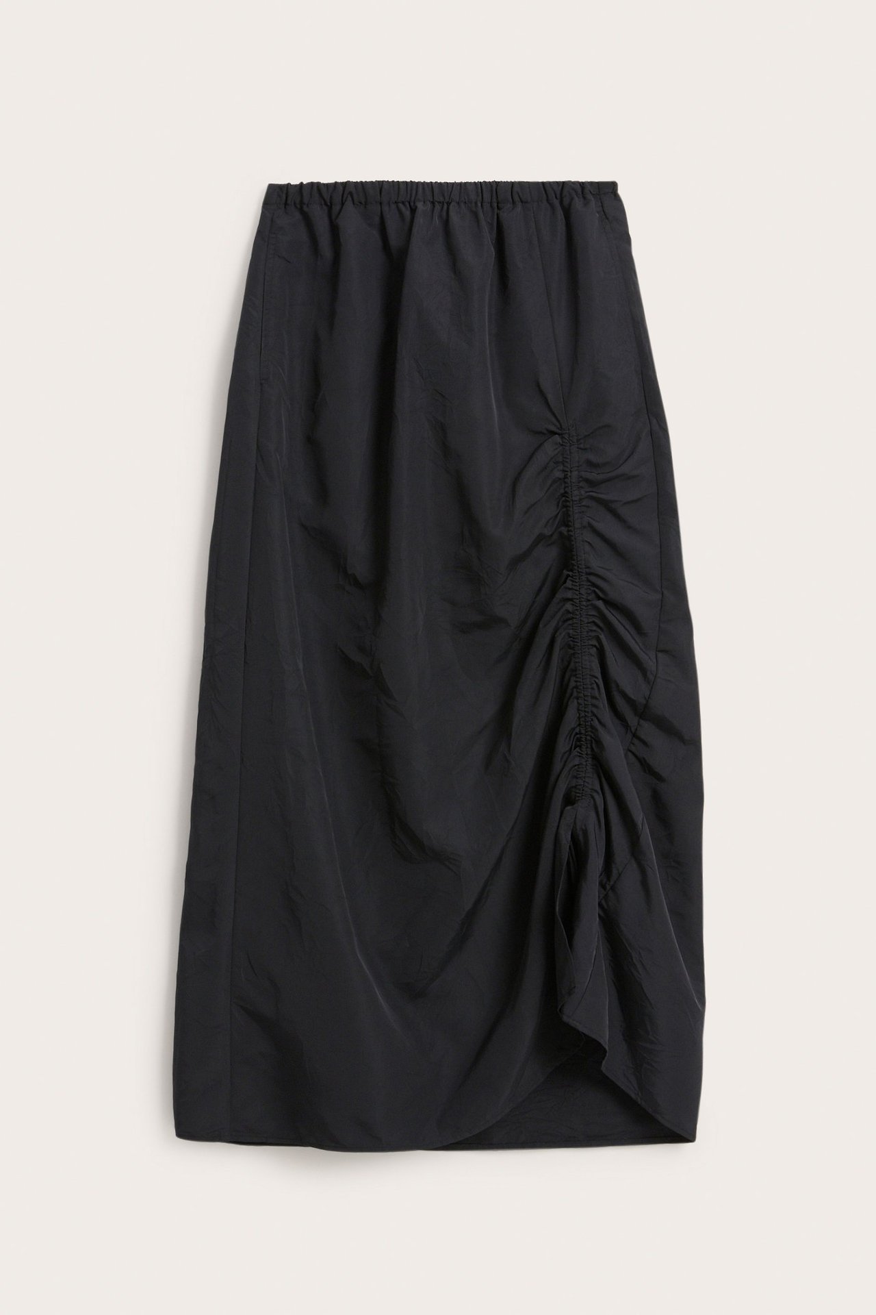 Framsida av en svart polyesterkjol med resår i midjan och justerbar draperingsdetalj på sidan.