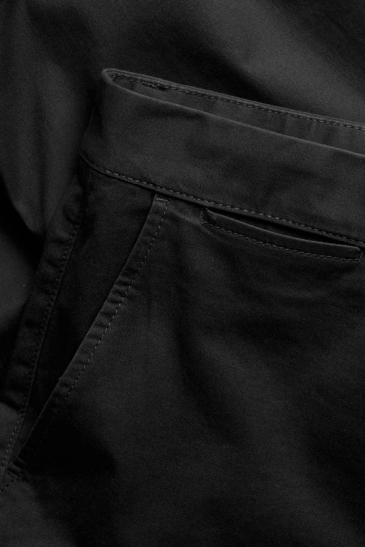Zbliżenie czarnych chinosów o regularnym kroju z bawełny z elastanem, pokazujące przednią kieszeń i pas.