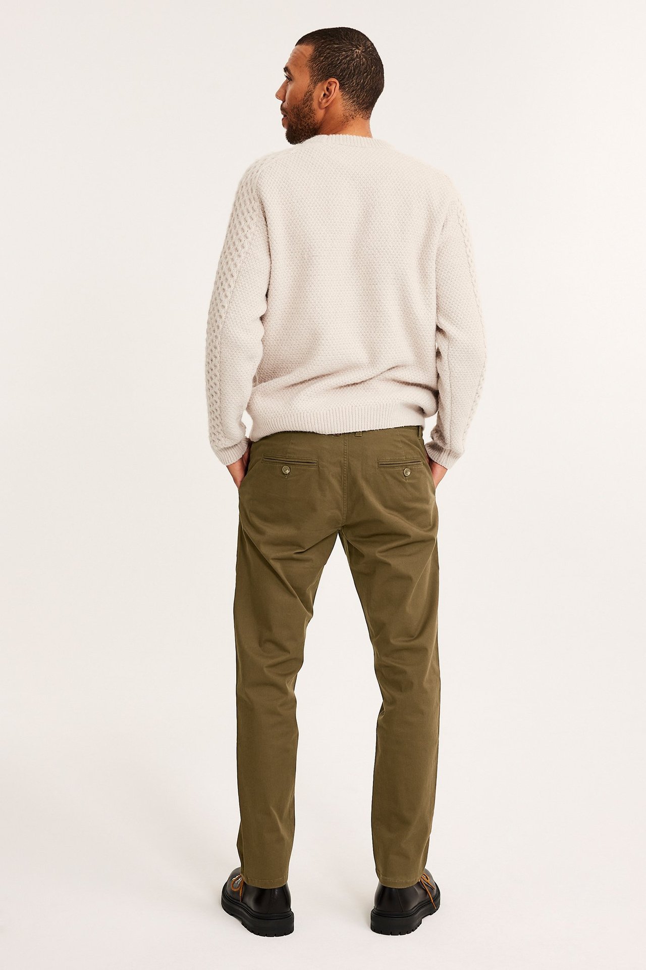 Mies takaa, ruskeat regular fit chinohousut, beige neulepusero ja mustat kengät.