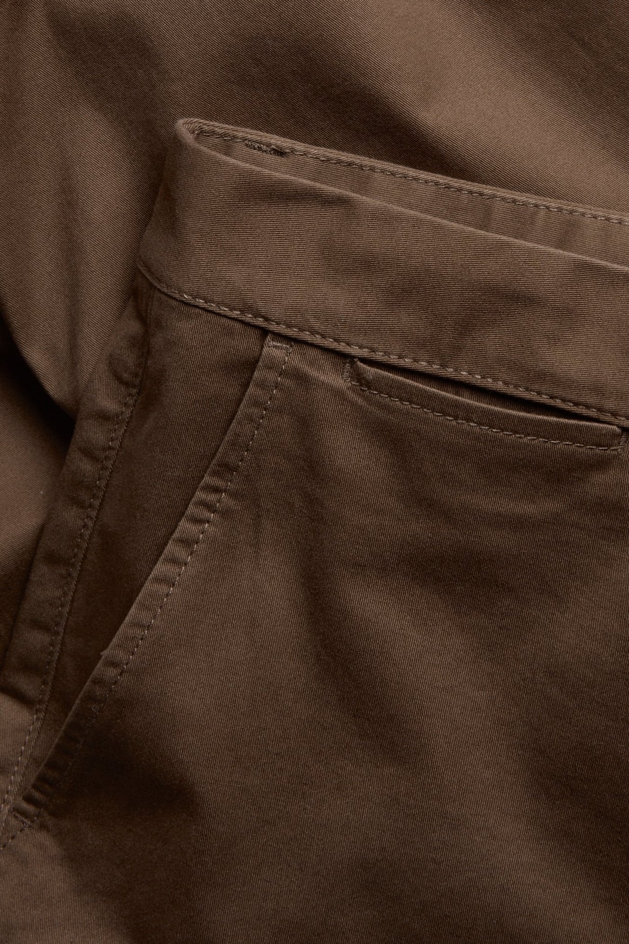 Zbliżenie na brązowe chinosy regular fit z bawełny z elastanem, widoczny pas i kieszeń.