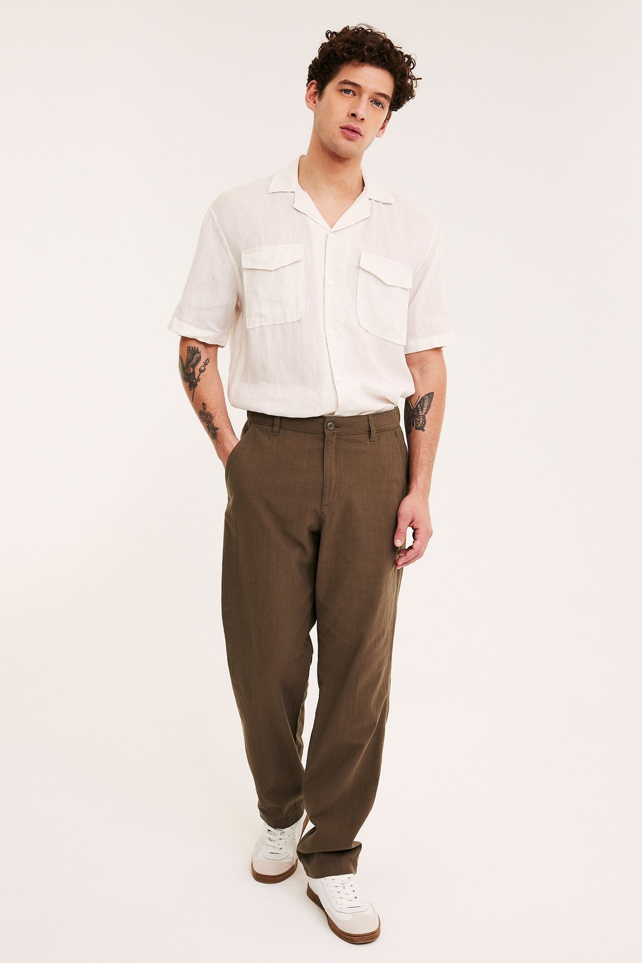Mies edestäpäin ruskeissa regular fit -chinoissa, valkoisessa lyhythihaisessa paidassa ja valkoisissa tennareissa.