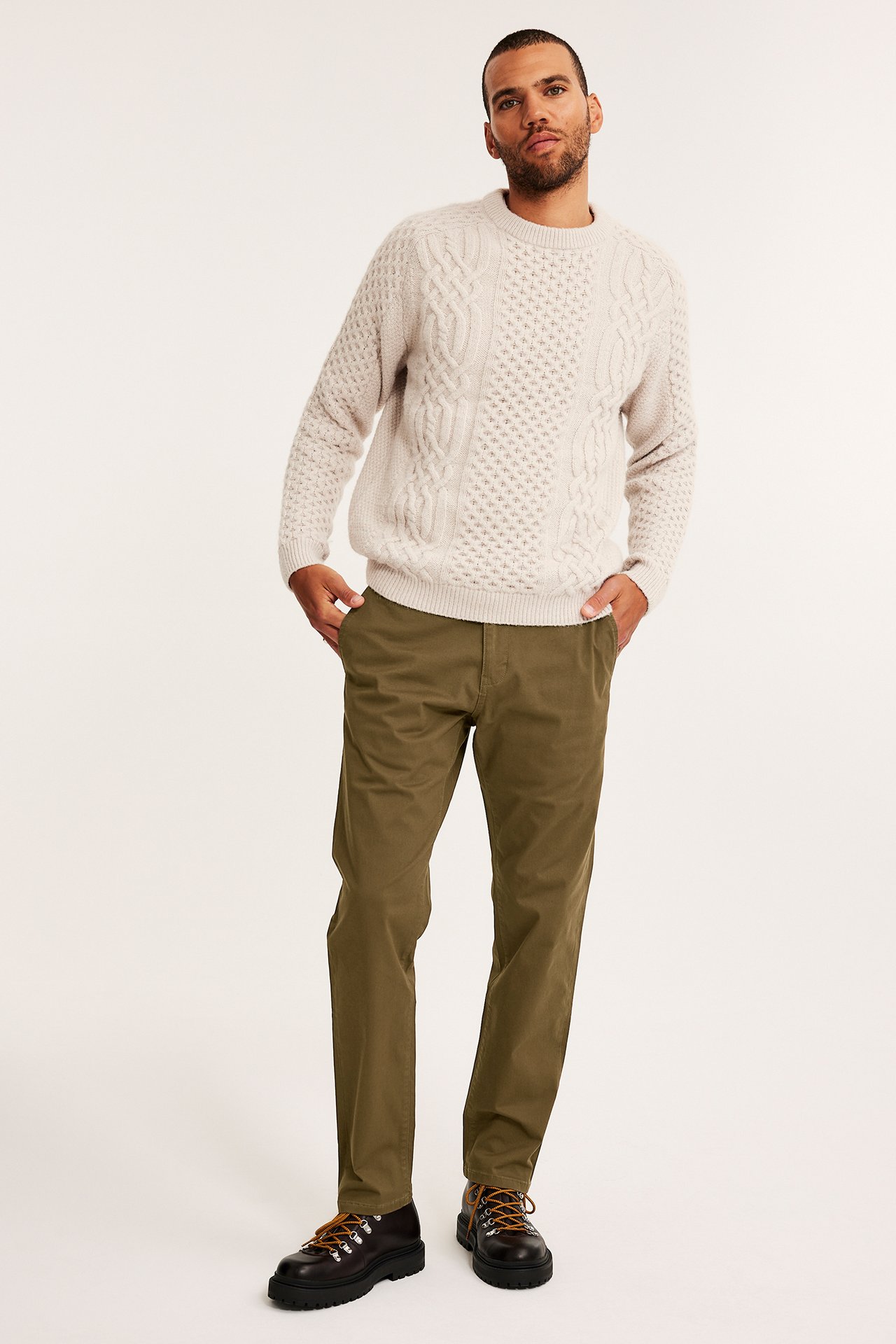 Mann har på seg brune regular fit chinos, lys beige flettet genser og mørkebrune sko.