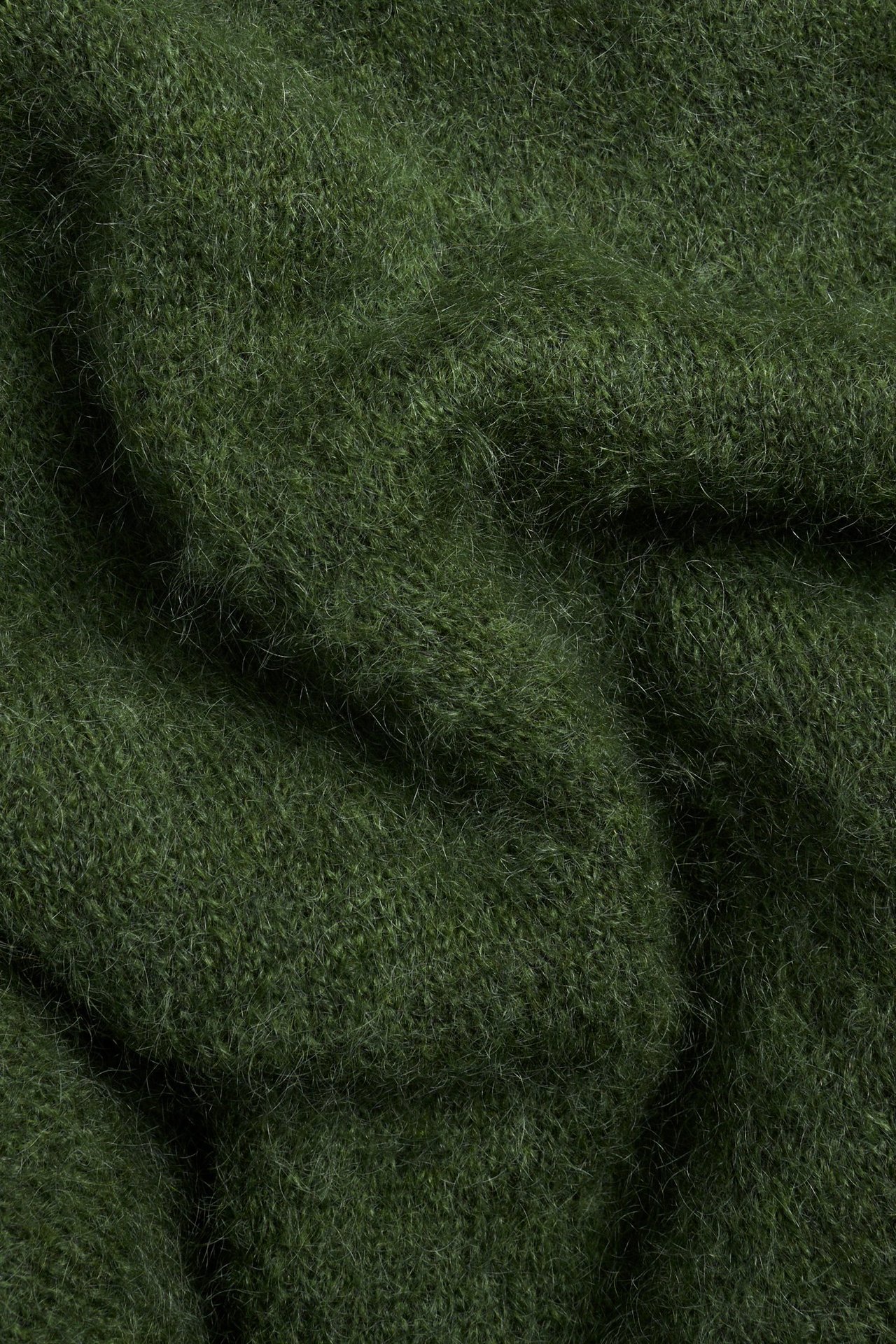 Zbliżenie zielonego, moherowego materiału swetra o puszystej, jednolitej dzianinowej fakturze.