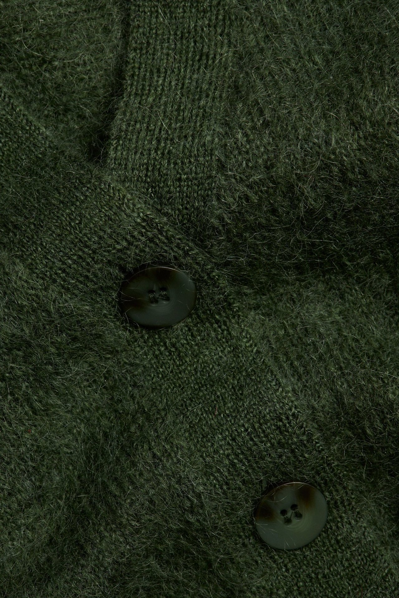 Zbliżenie zielonego puszystego swetra rozpinanego z dwoma ciemnymi guzikami.