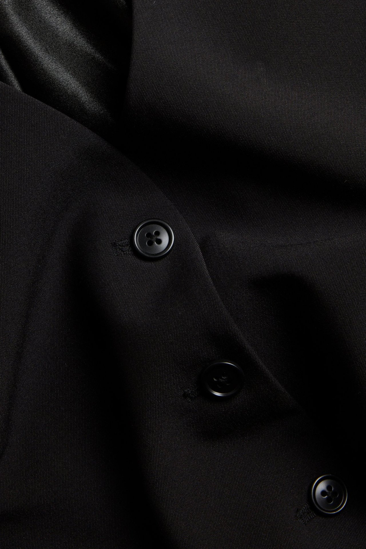 Zbliżenie czarnej, jednokolorowej kamizelki z czarnymi guzikami.