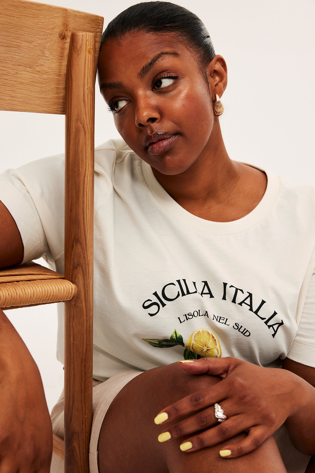Zbliżenie kobiety w białym T-shircie z nadrukiem "Sicilia Italia" i cytryny, złotych kolczykach i srebrnym pierścionku.