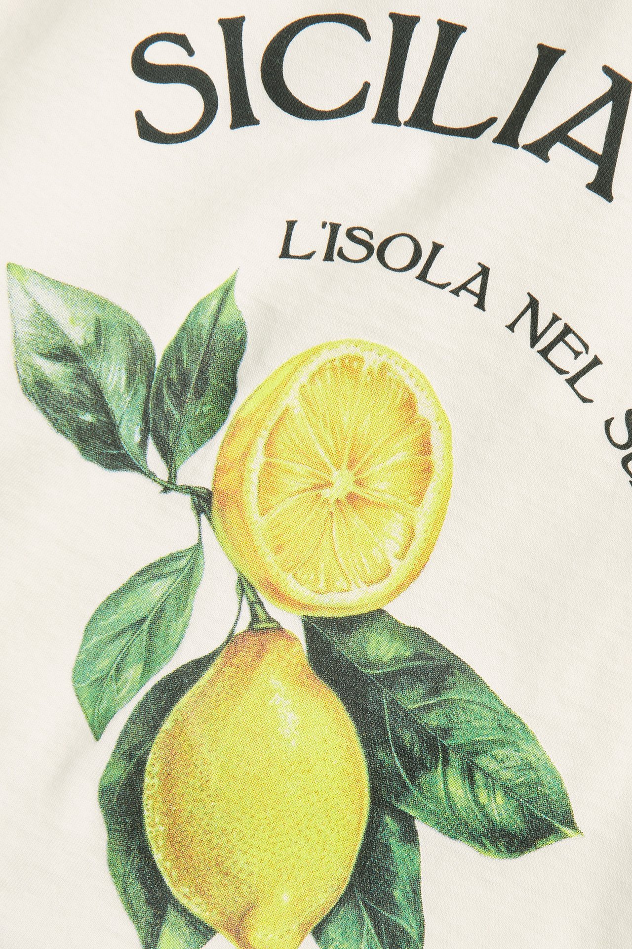 Zbliżenie białego bawełnianego T-shirtu z nadrukiem cytryn i tekstem 'SICILIA L'ISOLA NEL SOLE'.