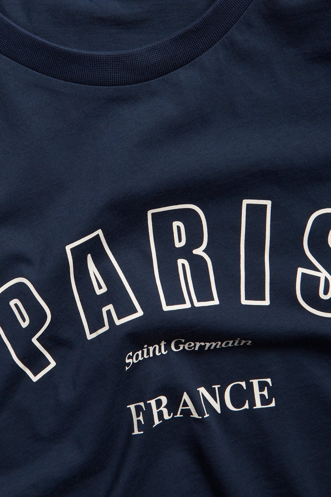 Närbild framifrån av en mörkblå bomulls-t-shirt med vitt "PARIS Saint Germain FRANCE" tryck.