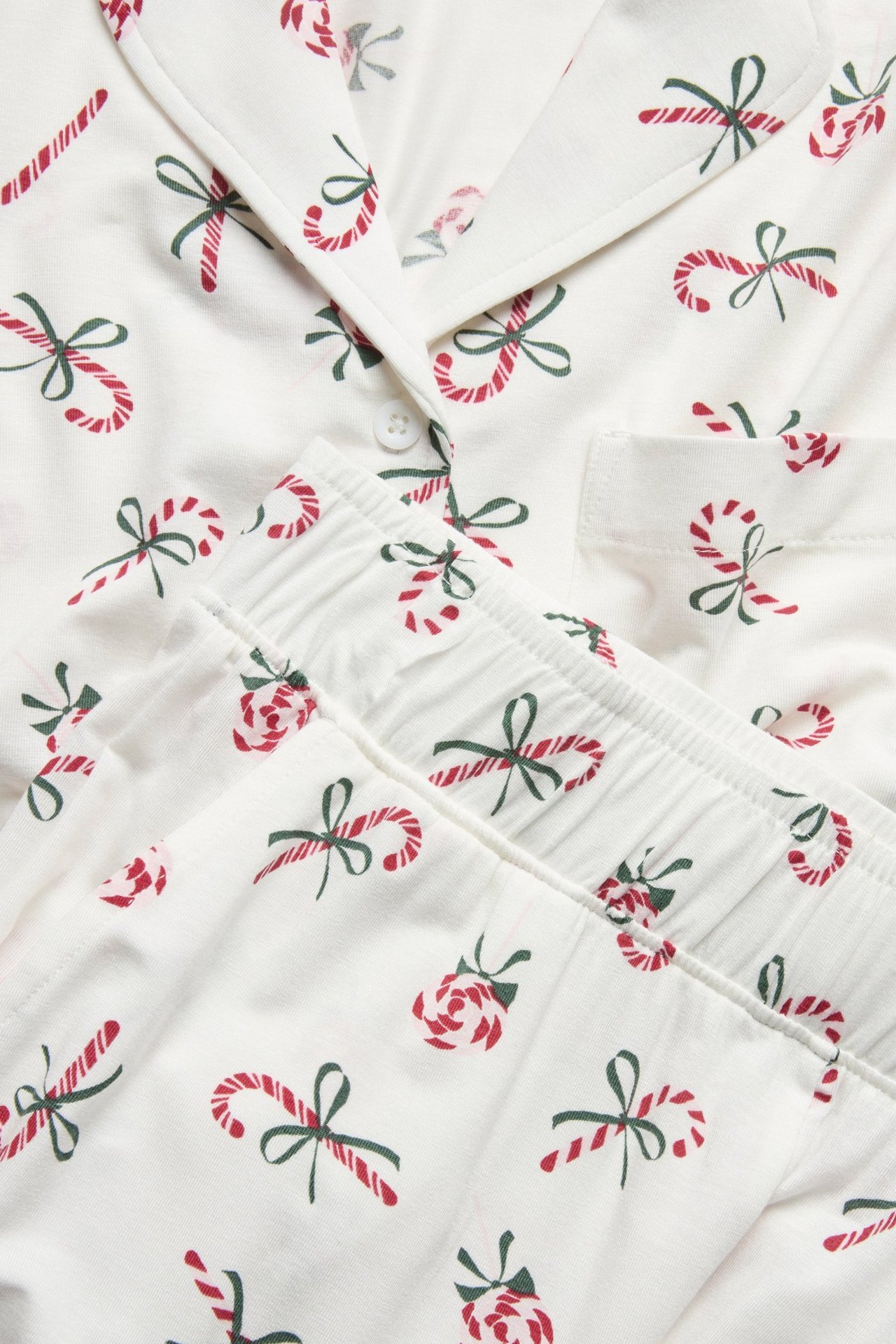 Nærbilde: Mønstret pyjamas i off-white, kraget topp, bukse med strikk, med røde godteristokker og grønne sløyfer.
