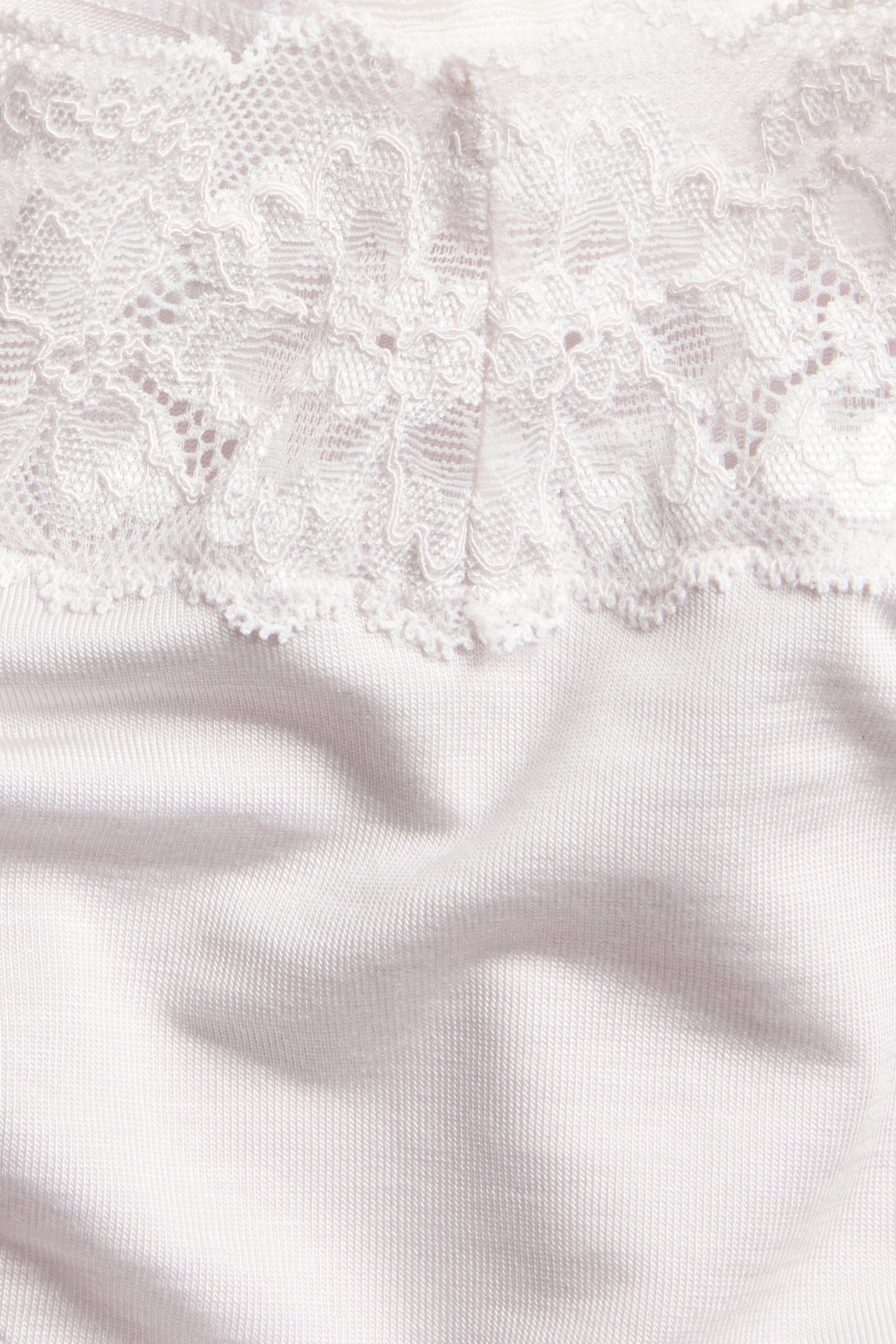 Zbliżenie jasnoróżowych majtek brazilian z mieszanki lyocellu z białą ozdobną koronkową krawędzią.