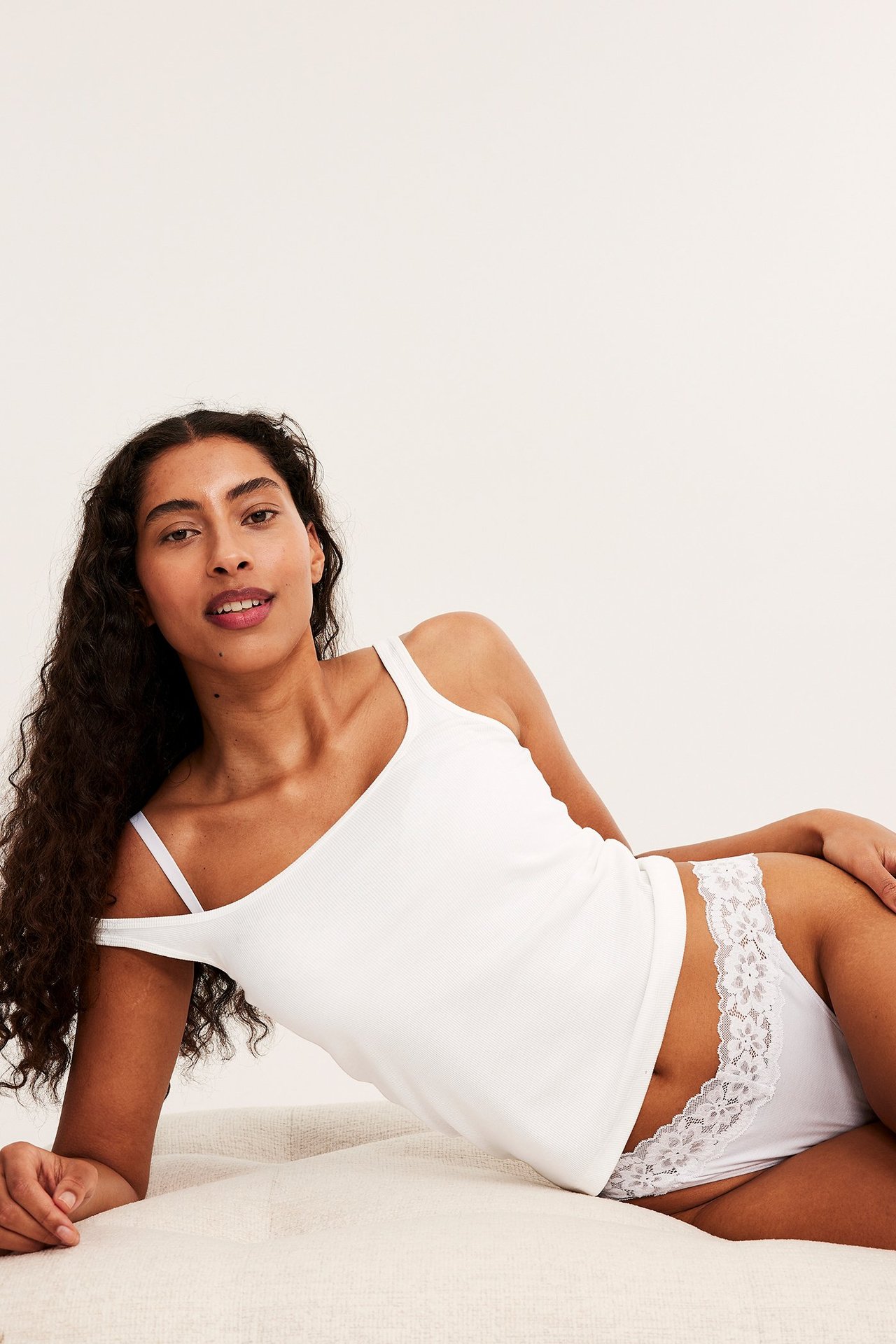 Sned framifrån-vy av en kvinna i vit lyocell stringtrosa med spetskant och ett vitt ribbat linne.