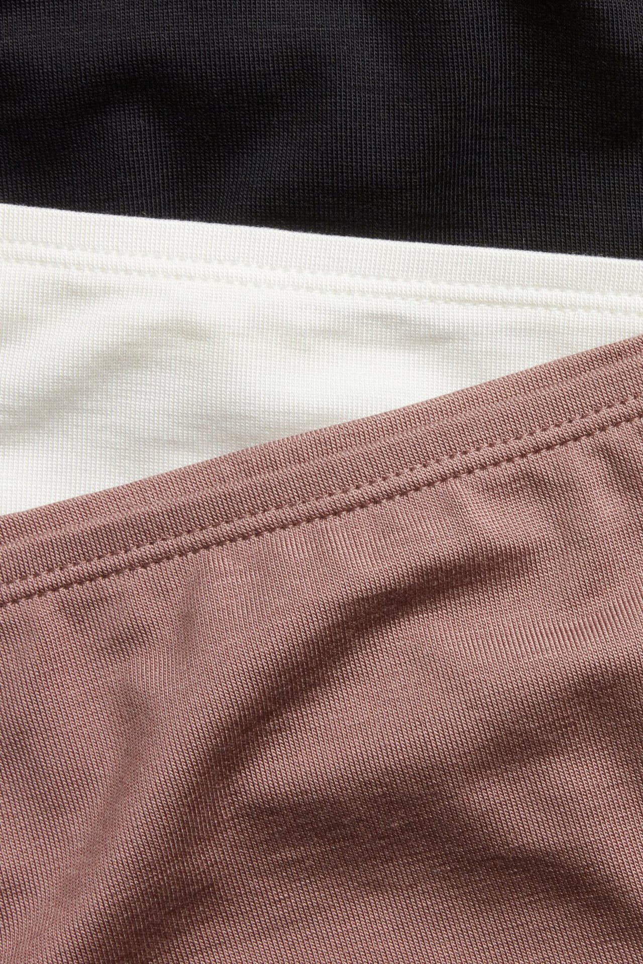 Zbliżenie trzech miękkich majtek z lyocellu: ciemnoróżowych, białych i czarnych, ułożonych w stos.