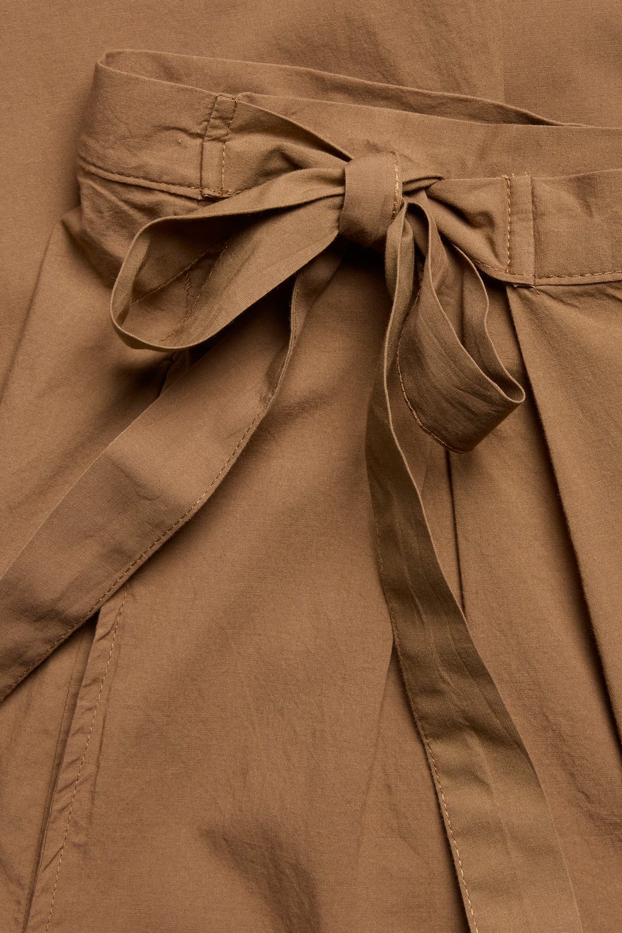 Zbliżenie brązowych spodni kopertowych z mieszanki bawełny i wiskozy z wiązaniem w talii.