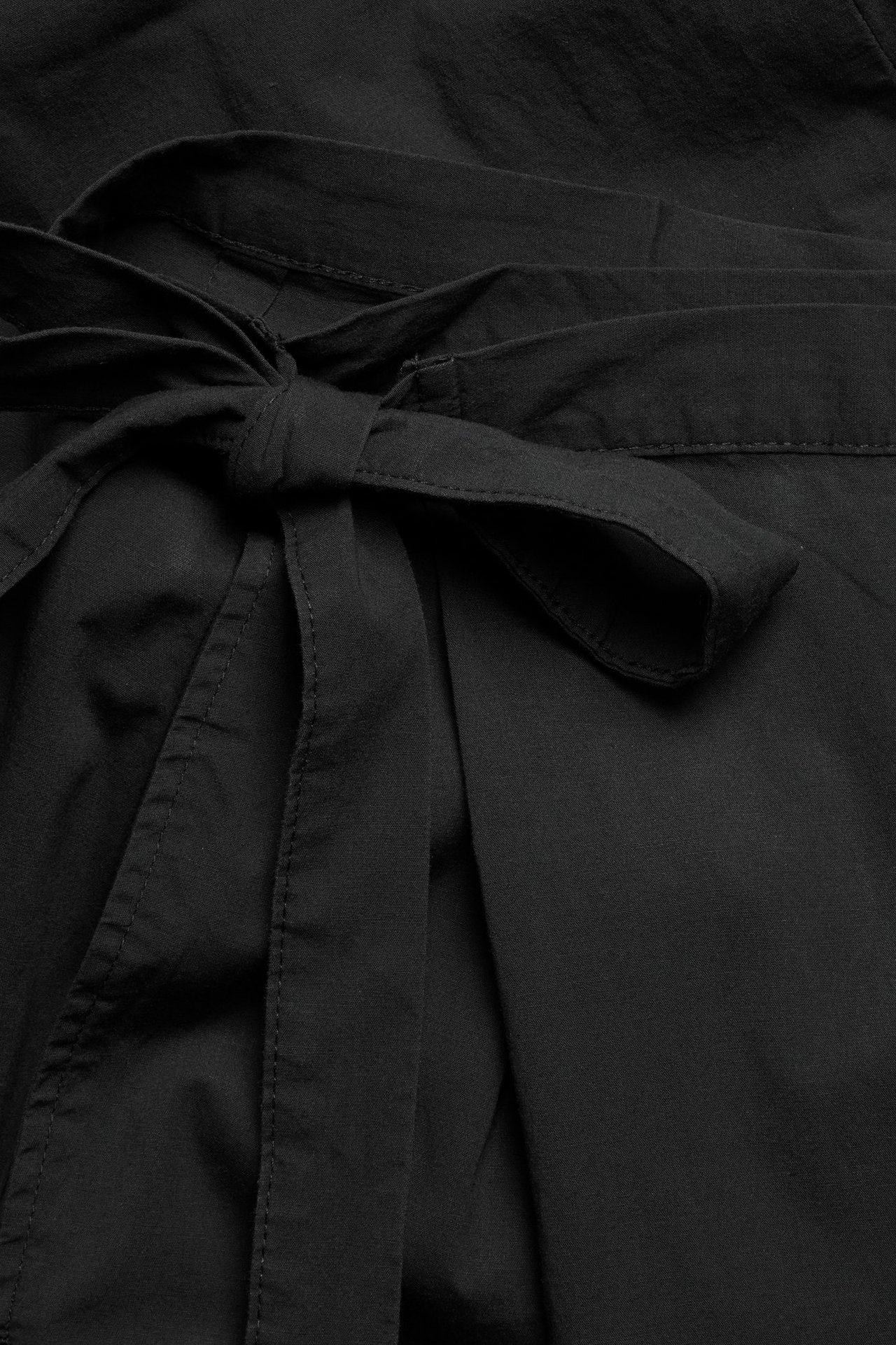 Zbliżenie czarnych spodni kopertowych z wiązaniem w talii, wykonanych z tkaniny.