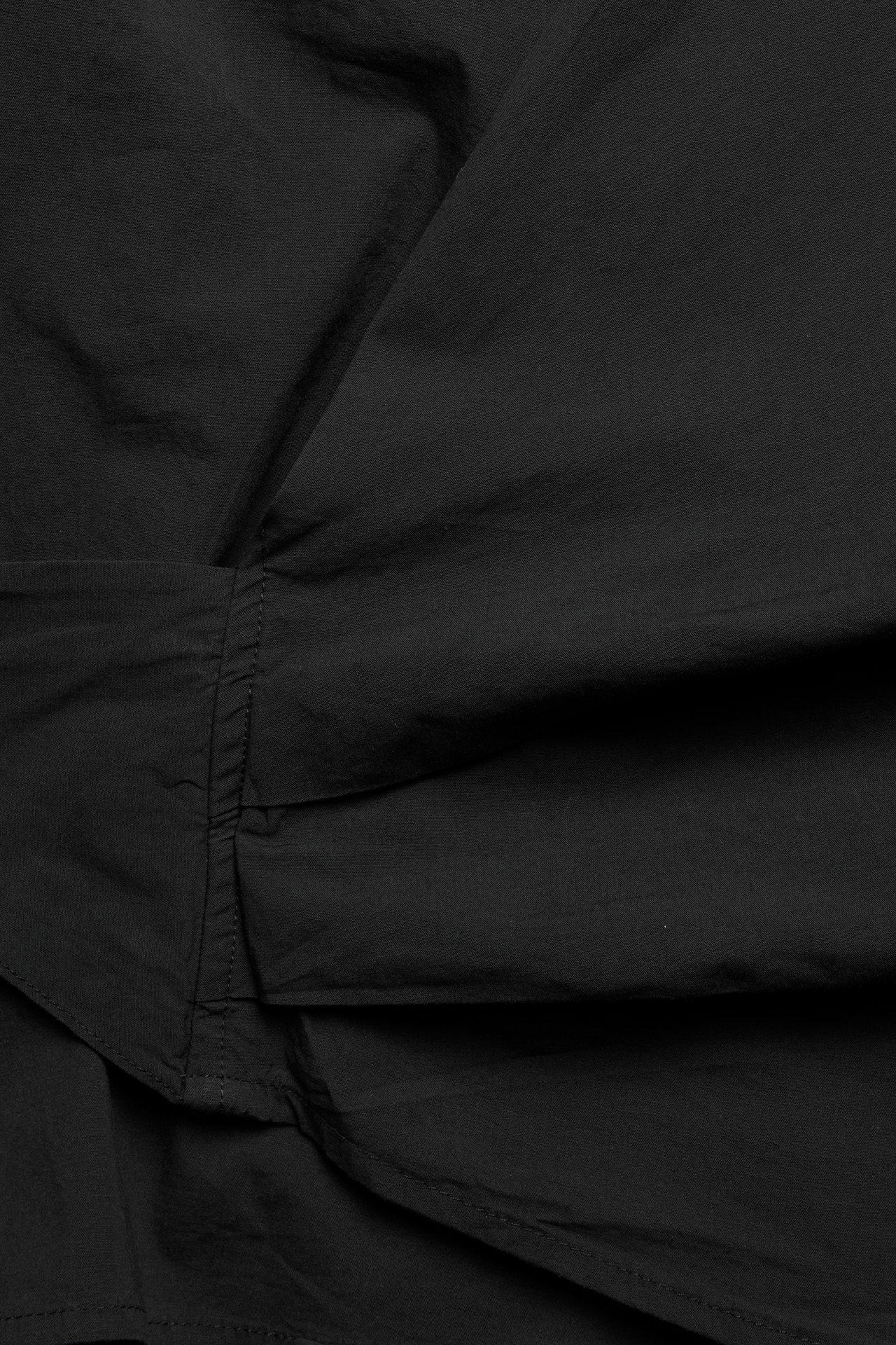 Zbliżenie czarnej, tkanej bluzki kopertowej z popeliny, ukazujące fakturę i detale szwów.