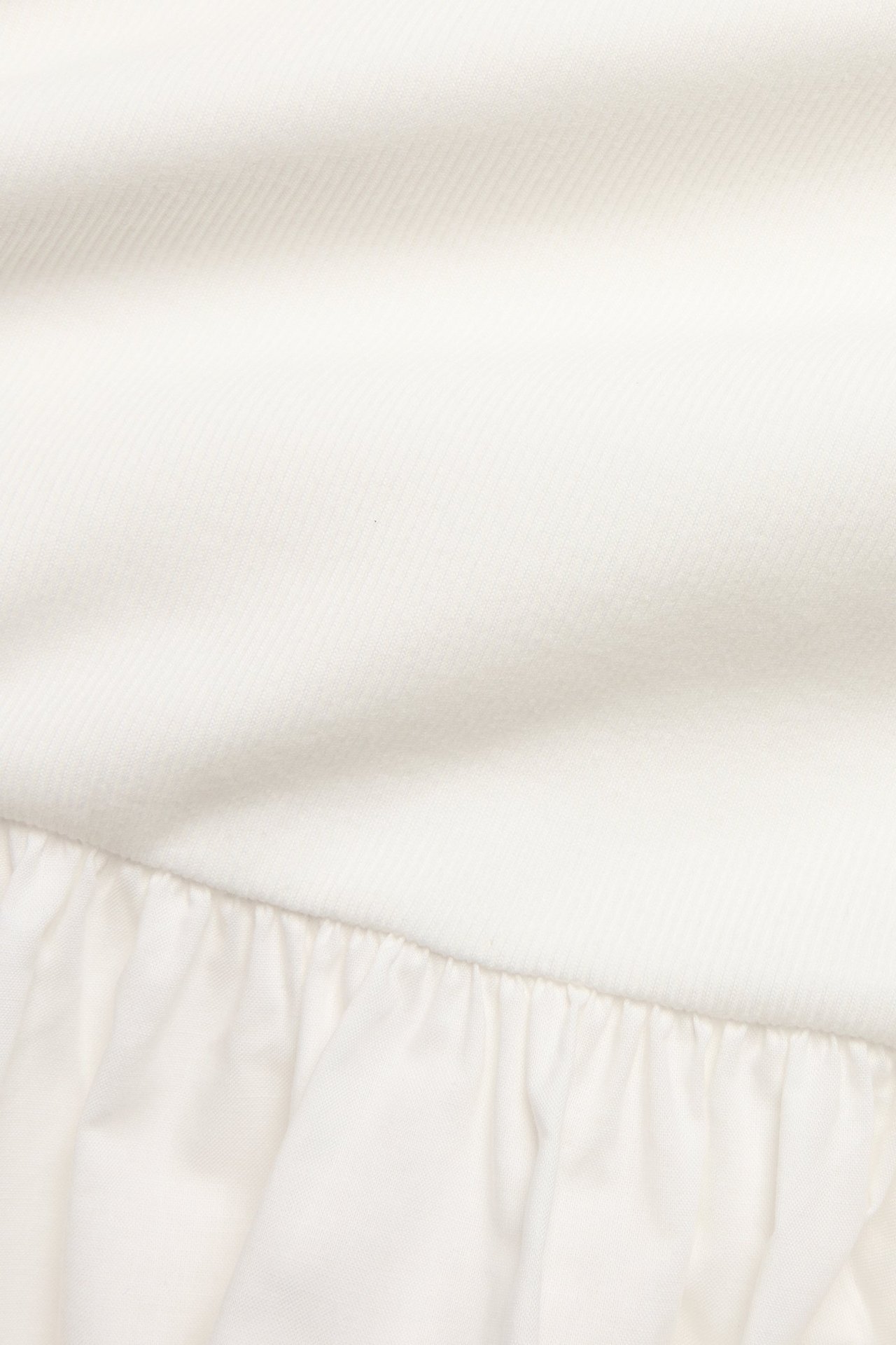 Zbliżenie sukienki w kolorze ecru z prążkowaną górą z dżerseju i marszczoną bawełnianą spódnicą.