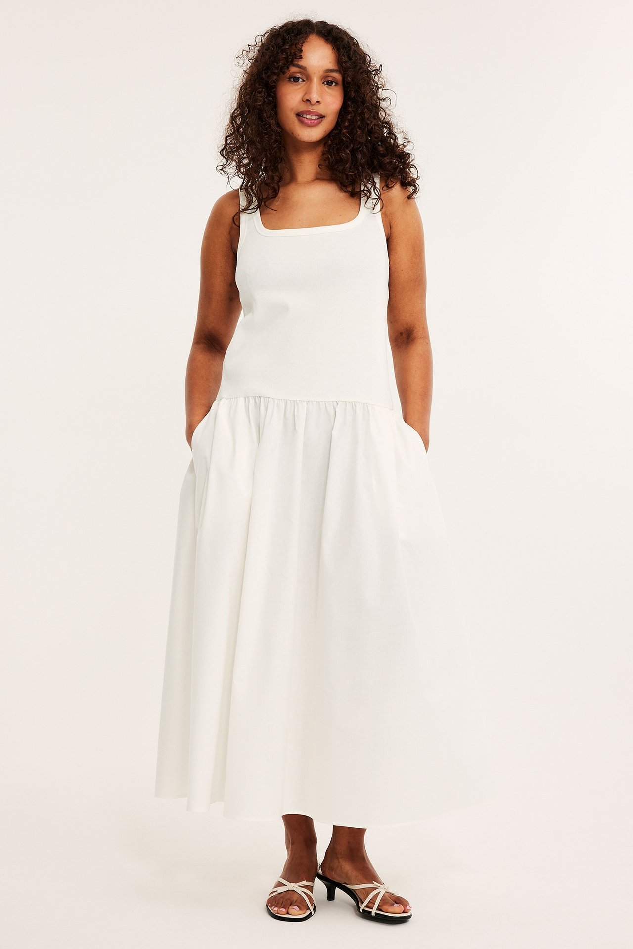 Frontalvisning: Kvinne i offwhite ribbet jerseykjole med rynket bomullsskjørt og hvite lavhælte sandaler.