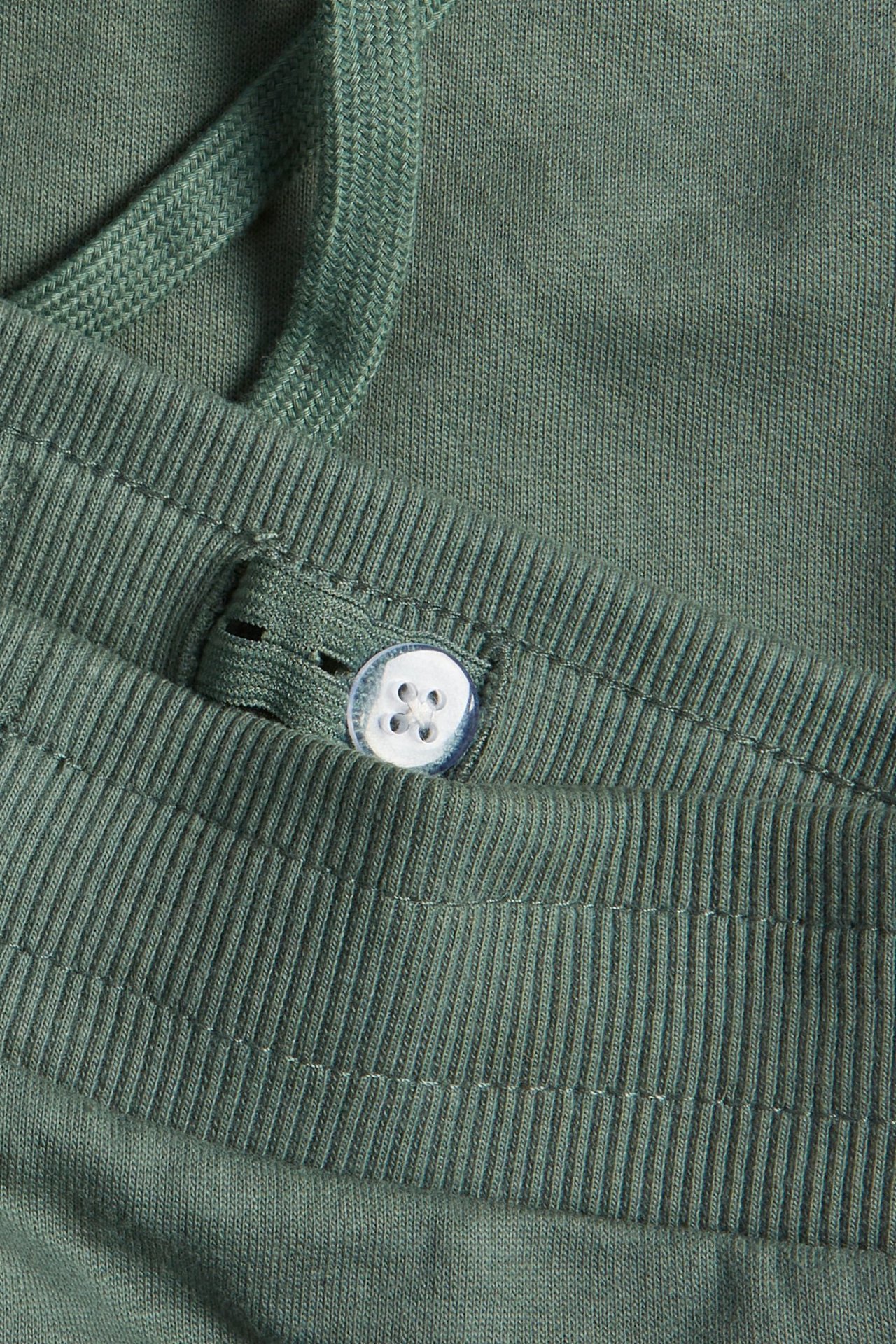 Zbliżenie na ciemnozielone spodnie dresowe z prążkowanym pasem, sznurkiem i białym guzikiem.