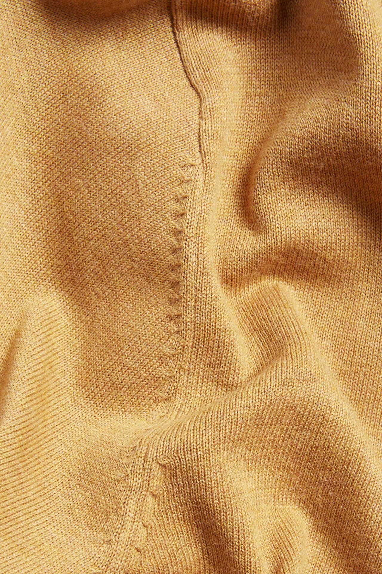 Zbliżenie żółtego melanżowego, drobno dzianego swetra ze 100% bawełny z ozdobnym szwem.