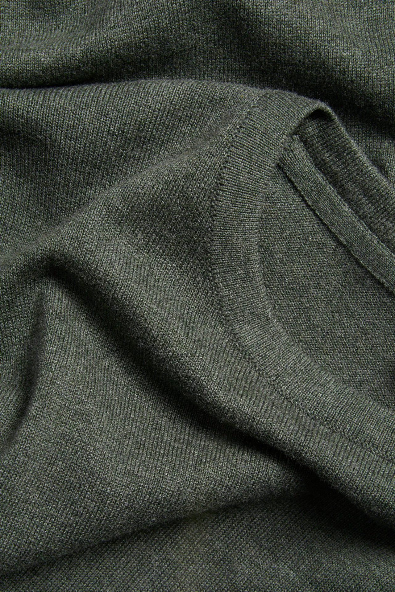 Zbliżenie ciemnozielonego melanżowego, drobno dzianego swetra bawełnianego z prążkowanym dekoltem.