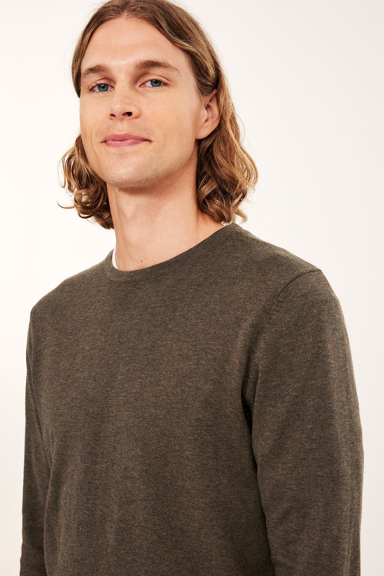 Lähikuva edestä miehestä, jolla on tummanruskea meleerattu hienoneulottu puuvillaneulepaita valkoisen t-paidan päällä.
