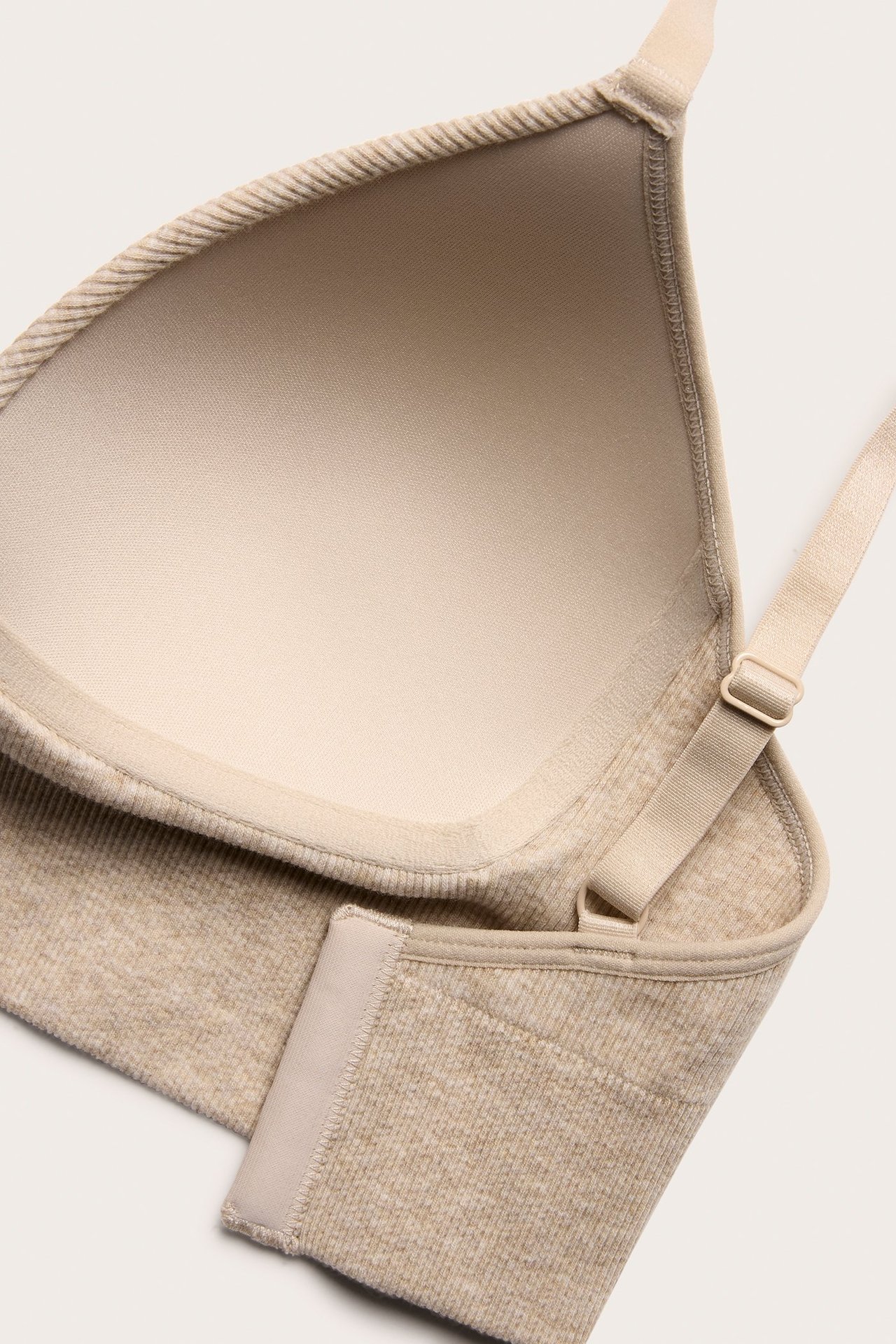 Zbliżenie, widok z góry, beżowego melanżowego biustonosza bezszwowego z prążkowaniem i regulowanymi ramiączkami.