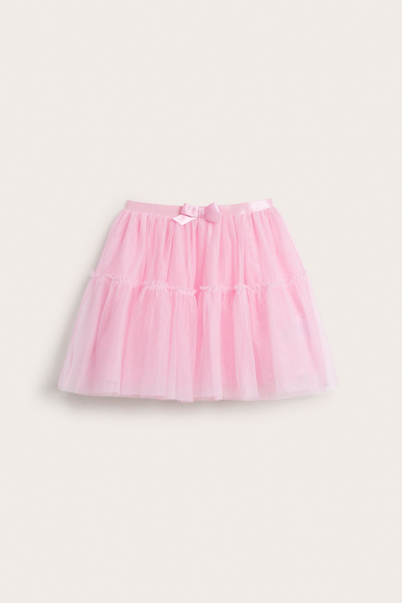 Framifrån, en rosa tyllkjol för barn med volanger och en liten rosett i midjan.