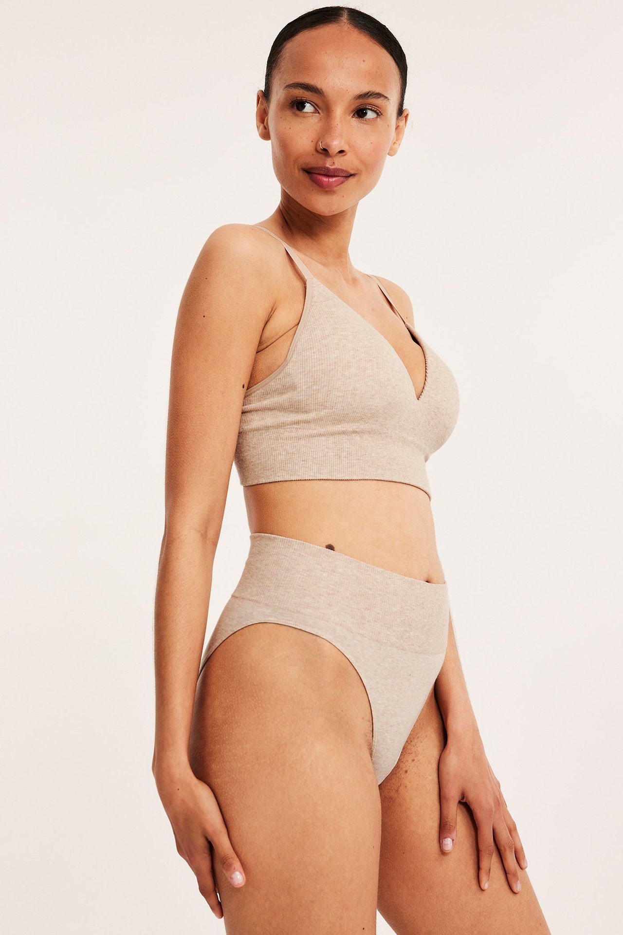 Sidebilde av en kvinne i beige melert ribbet Brazilian-truse og matchende bralette.
