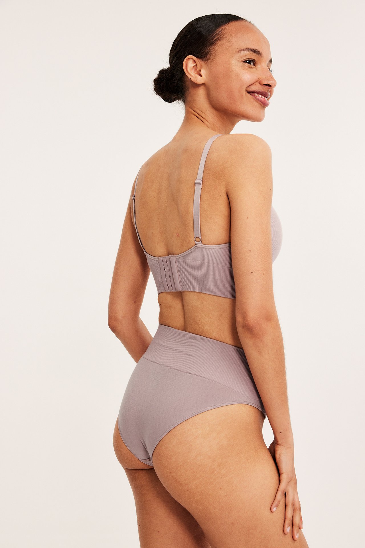 Sidevisning av en kvinne i dus rosa sømløs high-waist brazilian-truse og matchende BH.