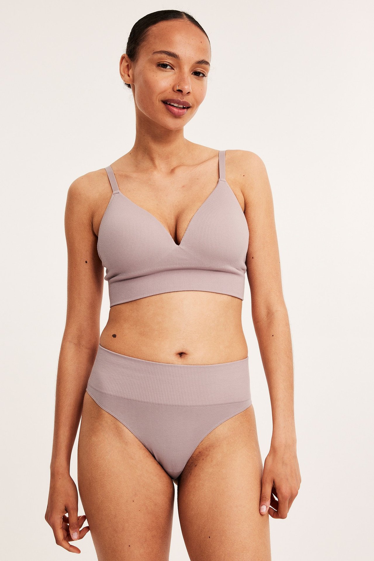 Frontbilde av en kvinne i rosa sømløs ribbet Brazilian-truse og matchende bralette.