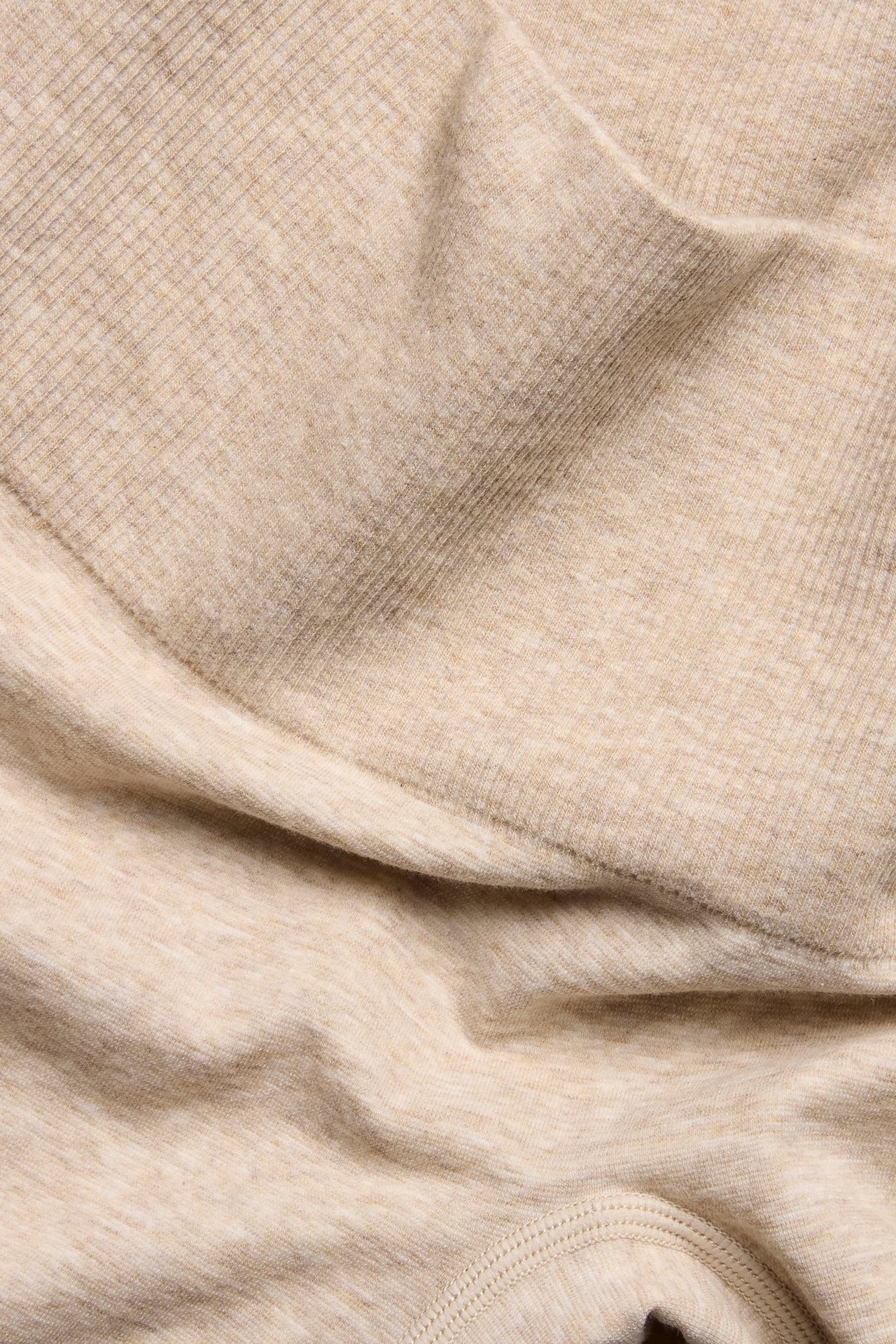 Zbliżenie beżowych melanżowych szortów z mieszanki bawełny z prążkowanym miękkim pasem.
