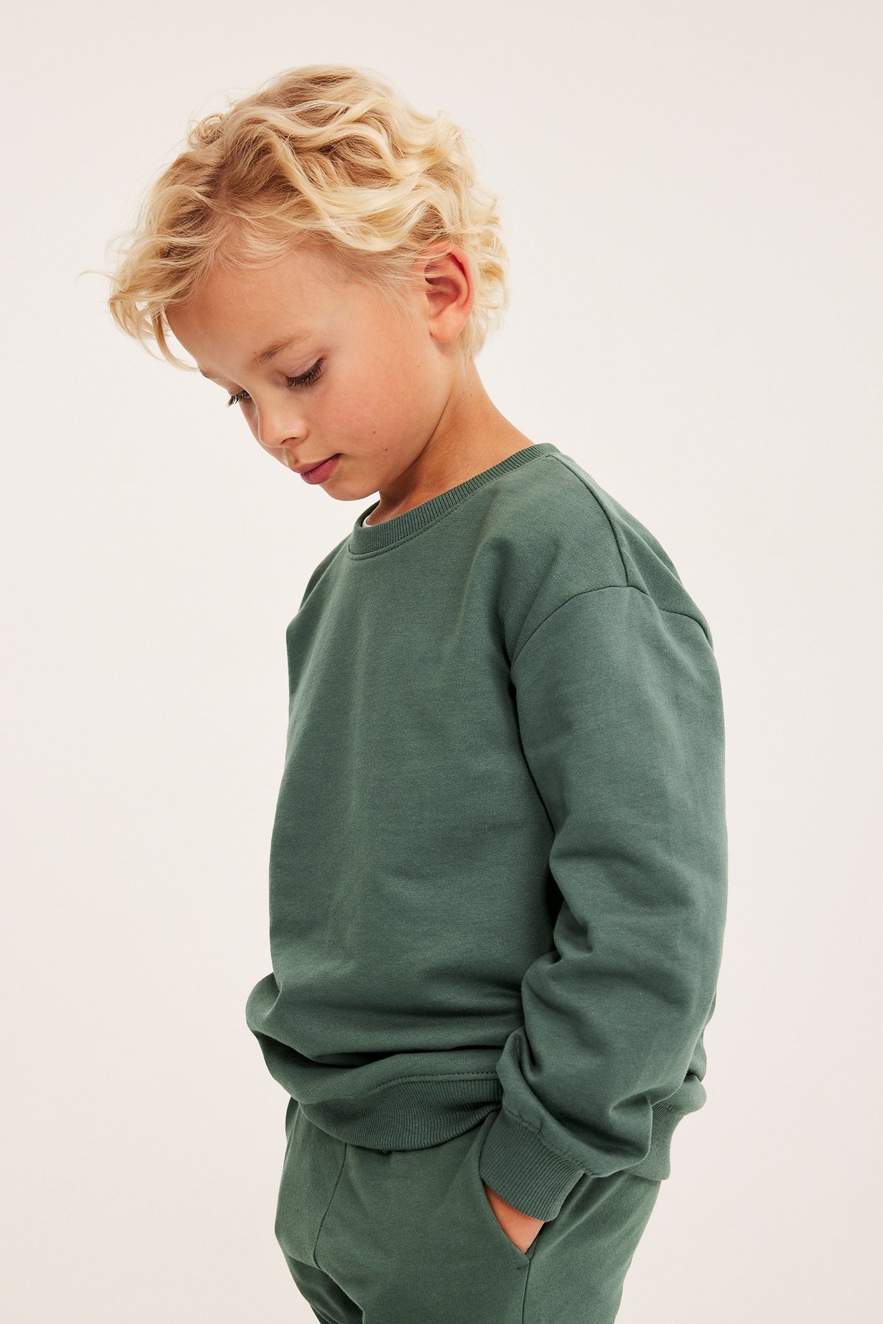 Sivukuva lapsesta yllään tummanvihreä puuvillainen collegepaita ja yhteensopivat collegehousut.