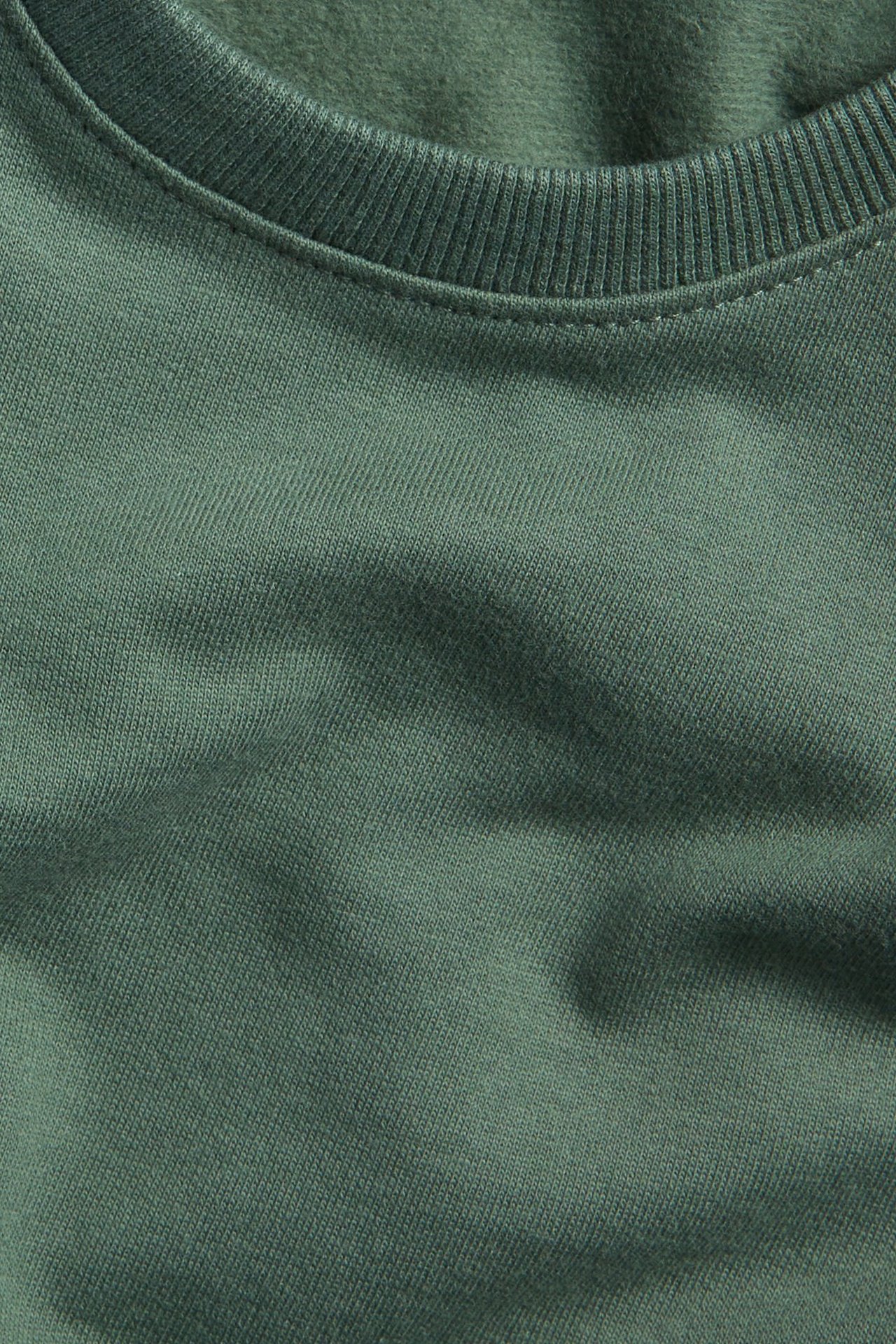 Zbliżenie na ciemnozieloną bawełnianą bluzę z okrągłym, prążkowanym dekoltem.