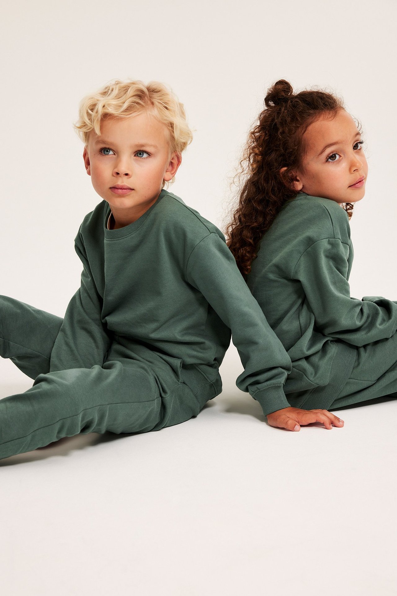 Widok z przodu: dwoje dzieci w pasujących ciemnozielonych bawełnianych bluzach z prążkowanymi detalami i spodniach.