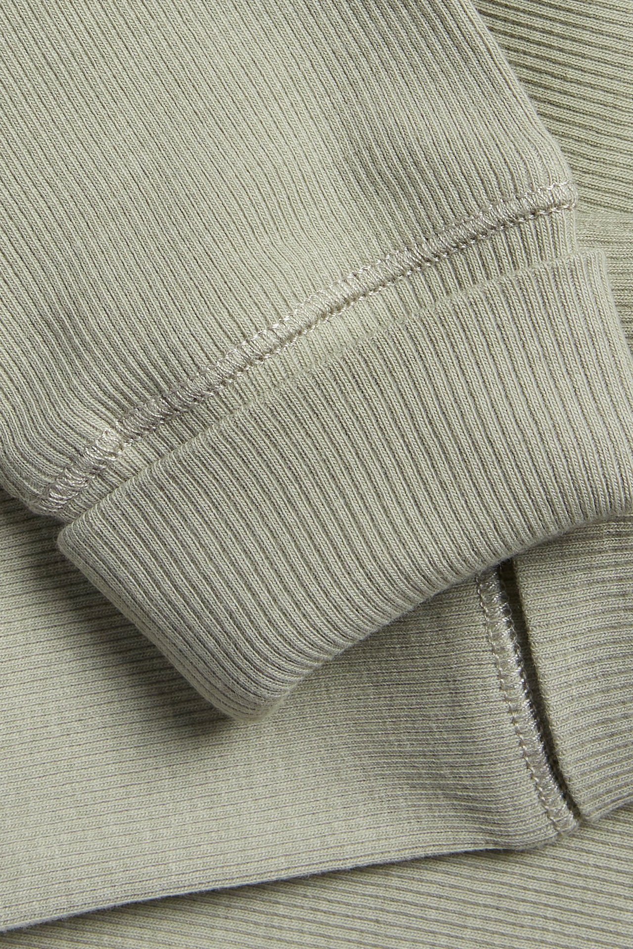 Zbliżenie zielonych prążkowanych legginsów, ukazujące teksturowany materiał bawełniany i podwinięty mankiet.